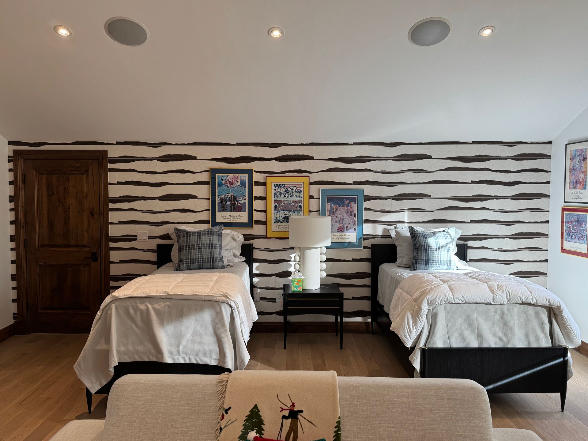 Two twin beds in a rustic bedroom with striped wall, wood dresser, and bedside lamp