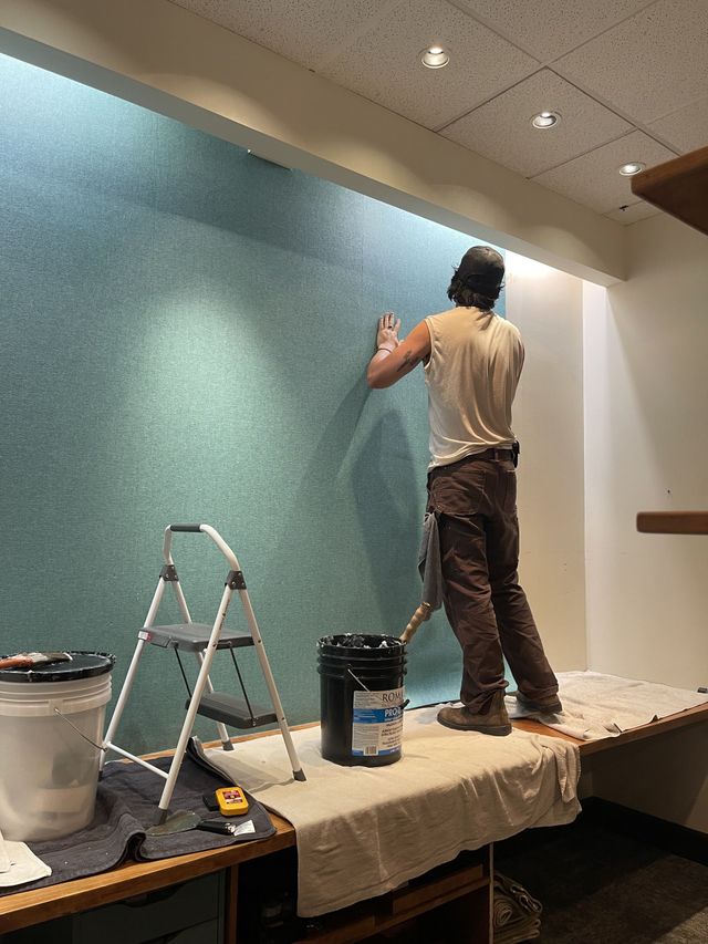 Person painting a teal wall on a ladder in a room under renovation