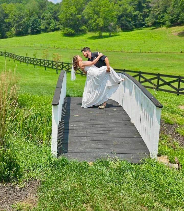 Couple in wedding attire kissing on a small bridge in a green countryside field