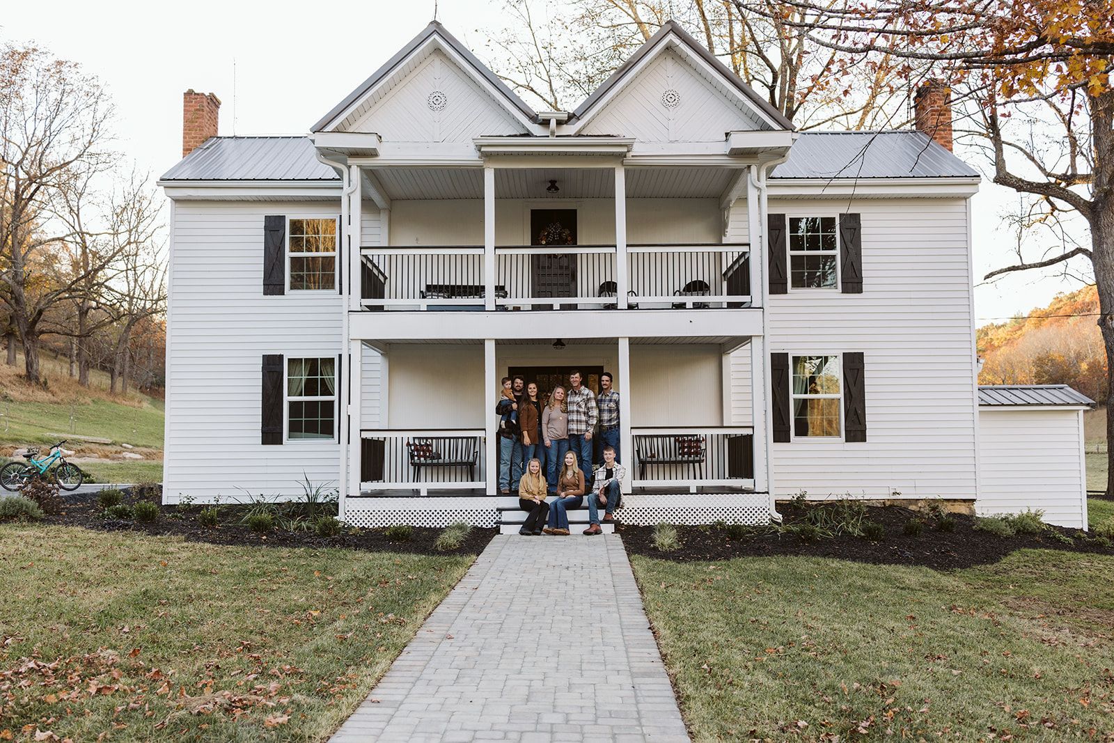 A group of people are standing on the porch of a large white house.