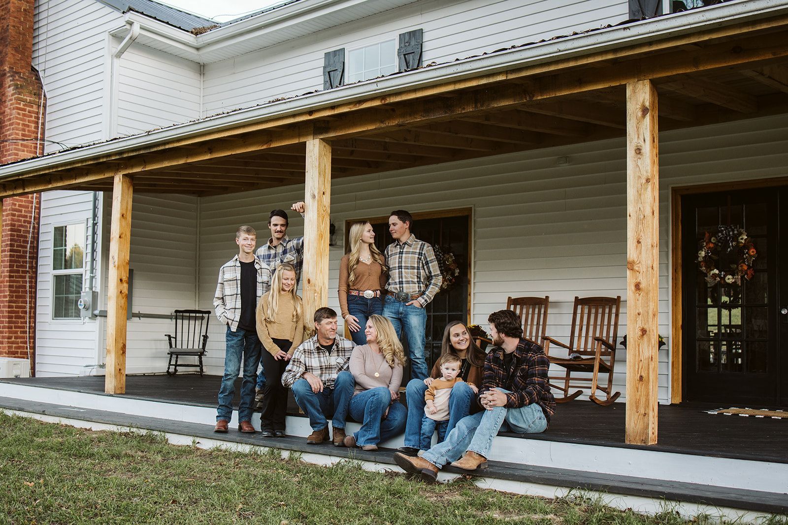 Group of people sitting and standing on a wooden porch in front of a house, posing together.