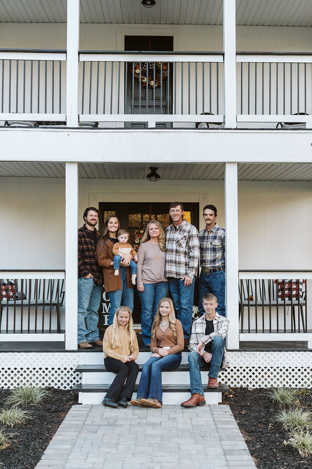 A large family is posing for a picture on the porch of their house.