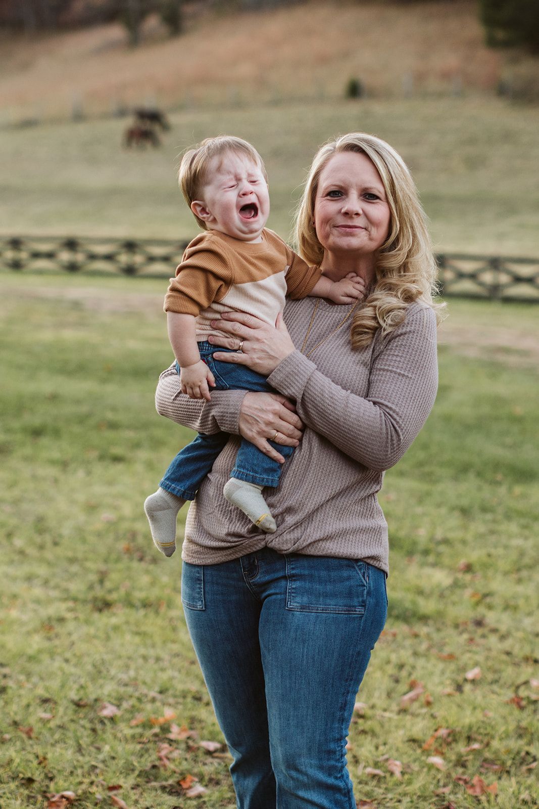 A woman is holding a crying baby in her arms in a field.