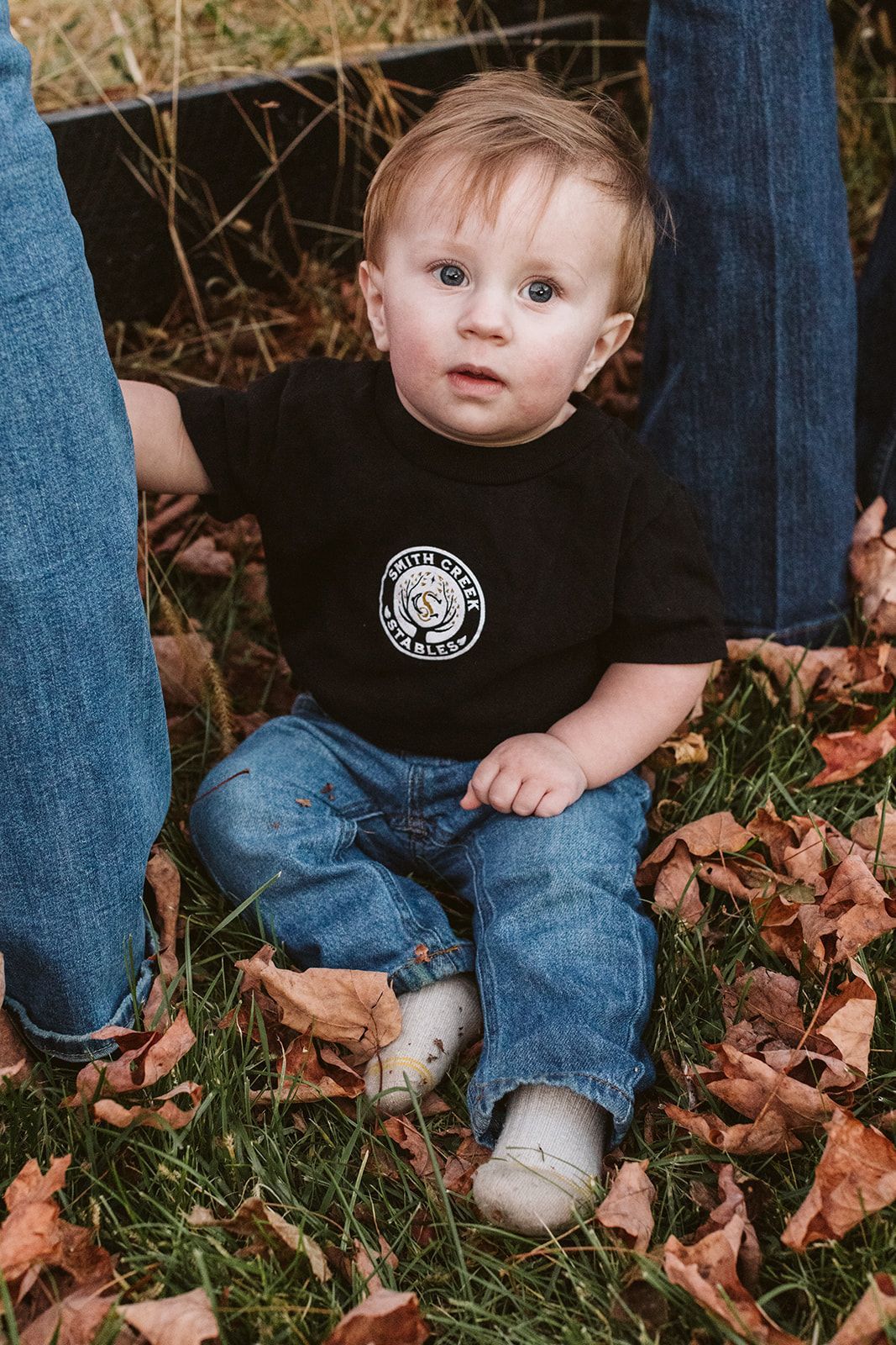 A little boy wearing a black shirt is sitting in the grass