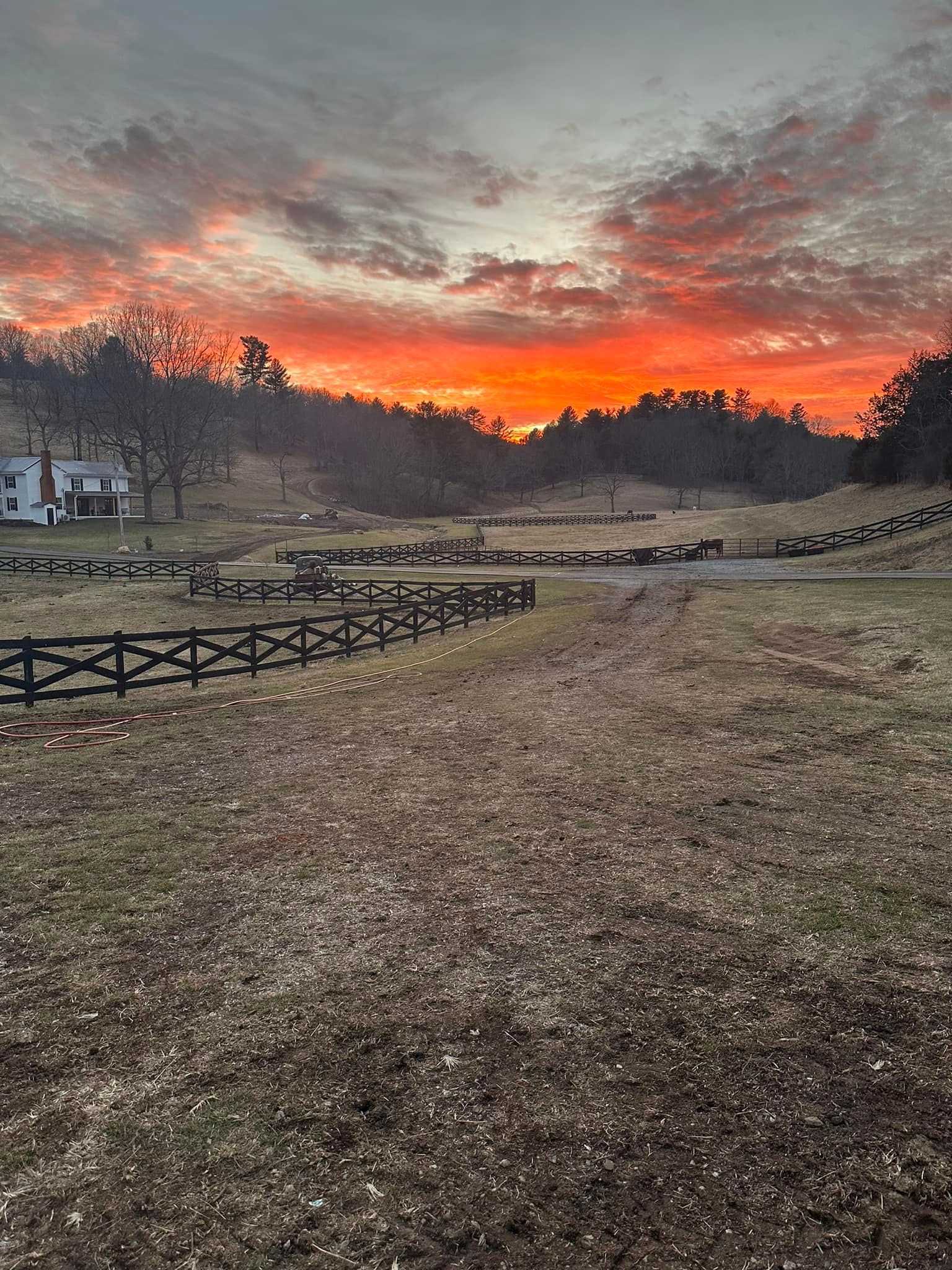 A sunset over a field with a wooden fence in the foreground.