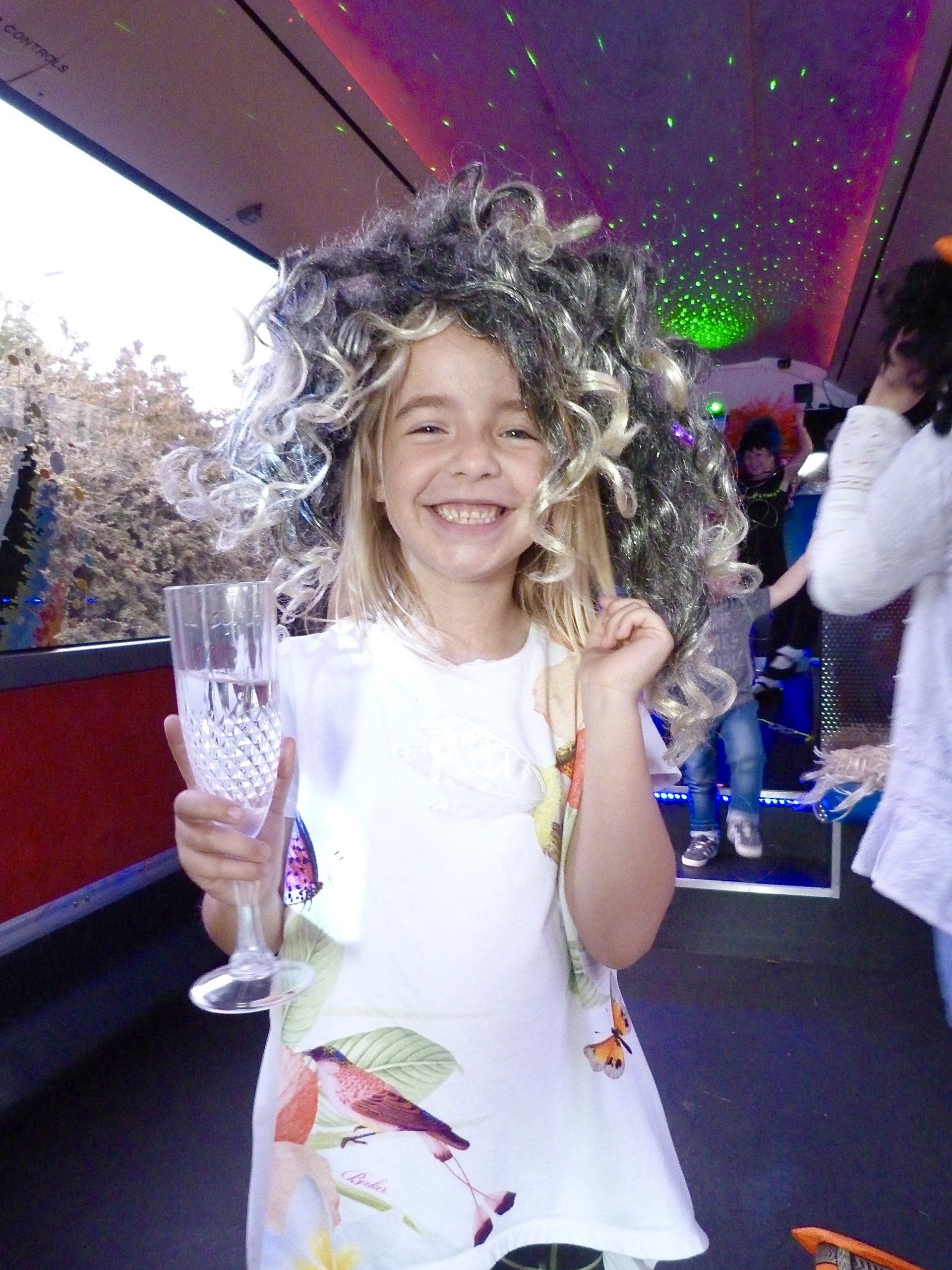 A little girl wearing a wig and holding a glass that says ivan
