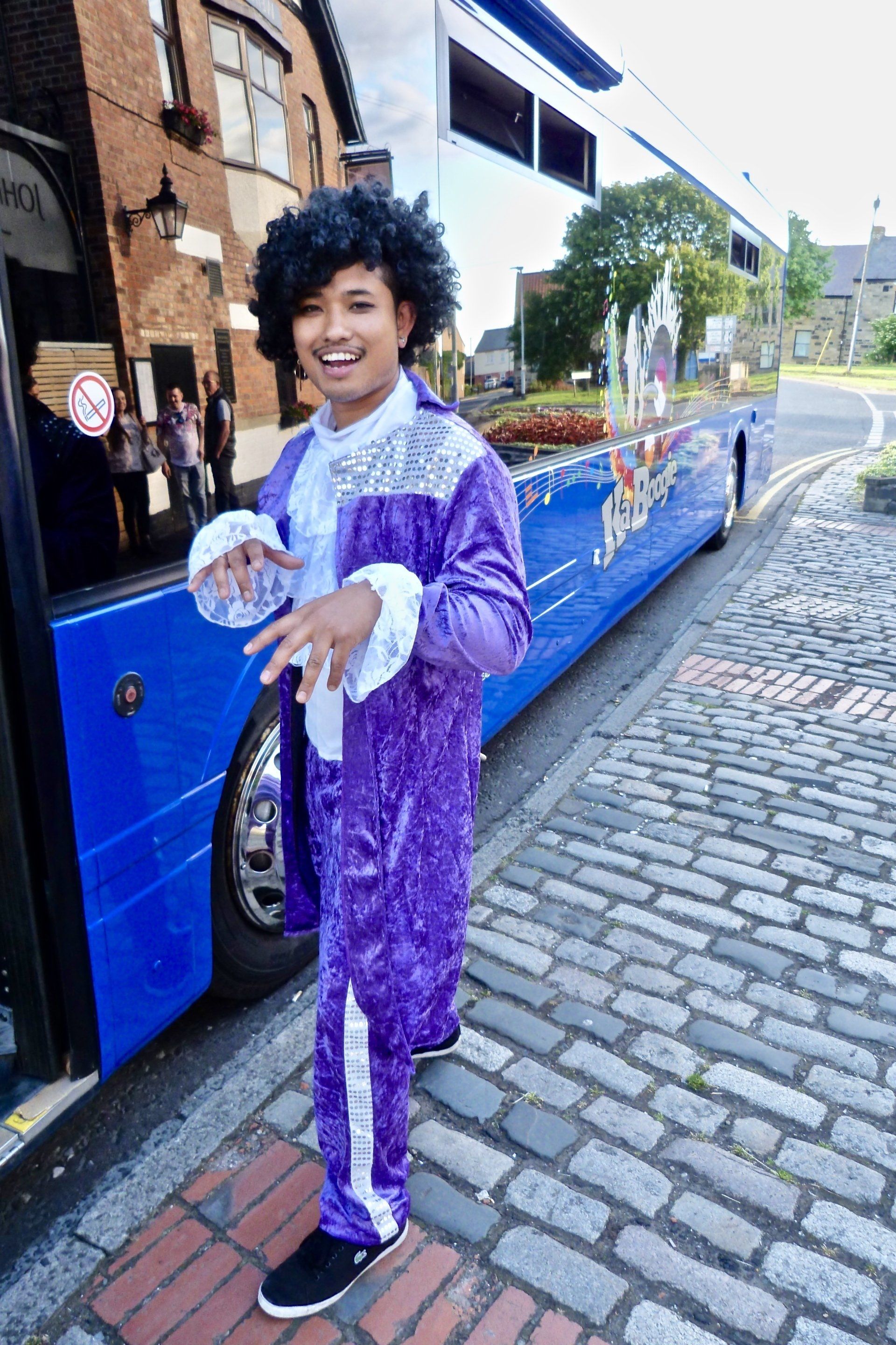 A young boy in a purple suit is standing in front of a blue bus.