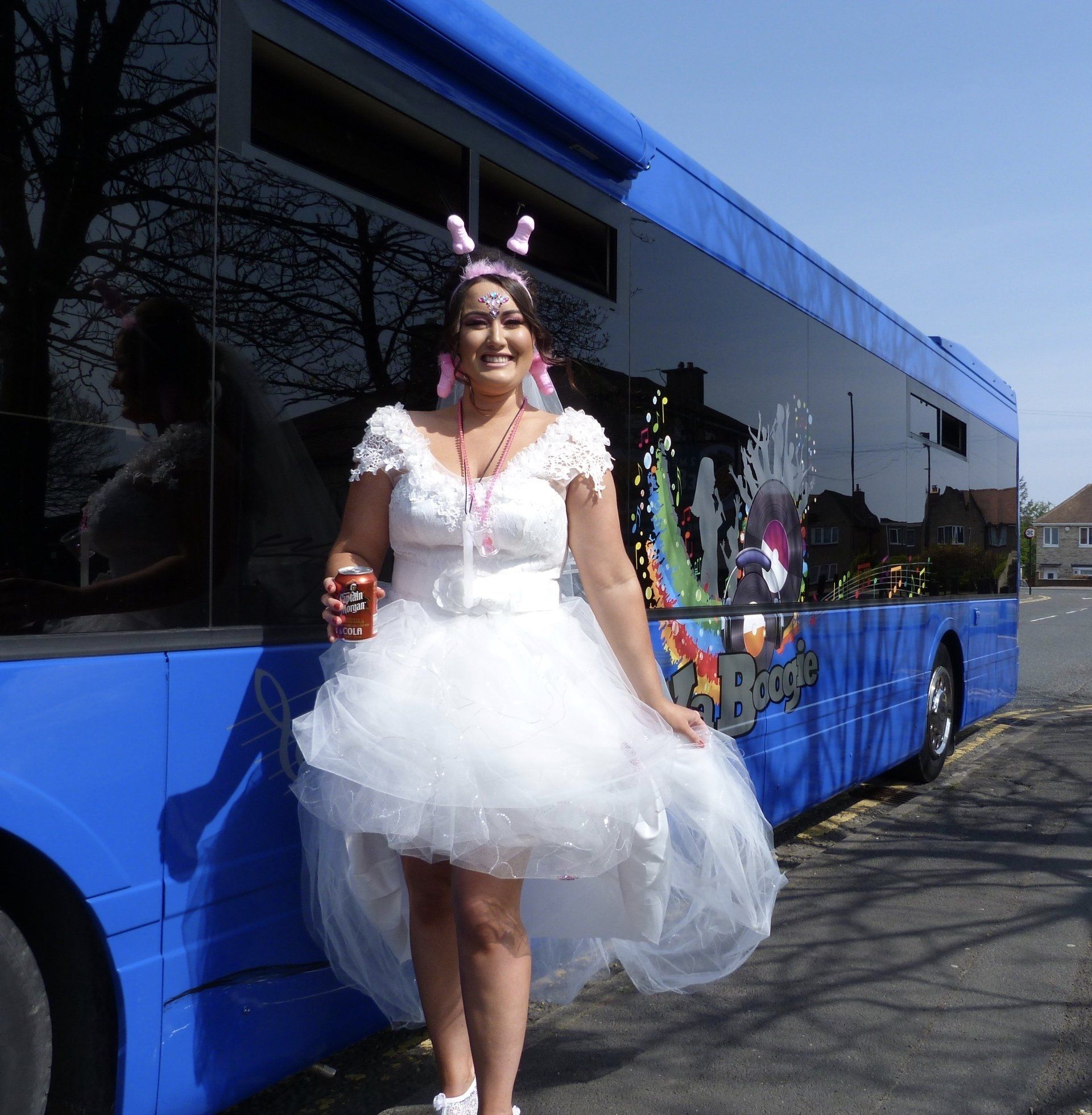 A woman in a white dress is standing in front of a blue bus