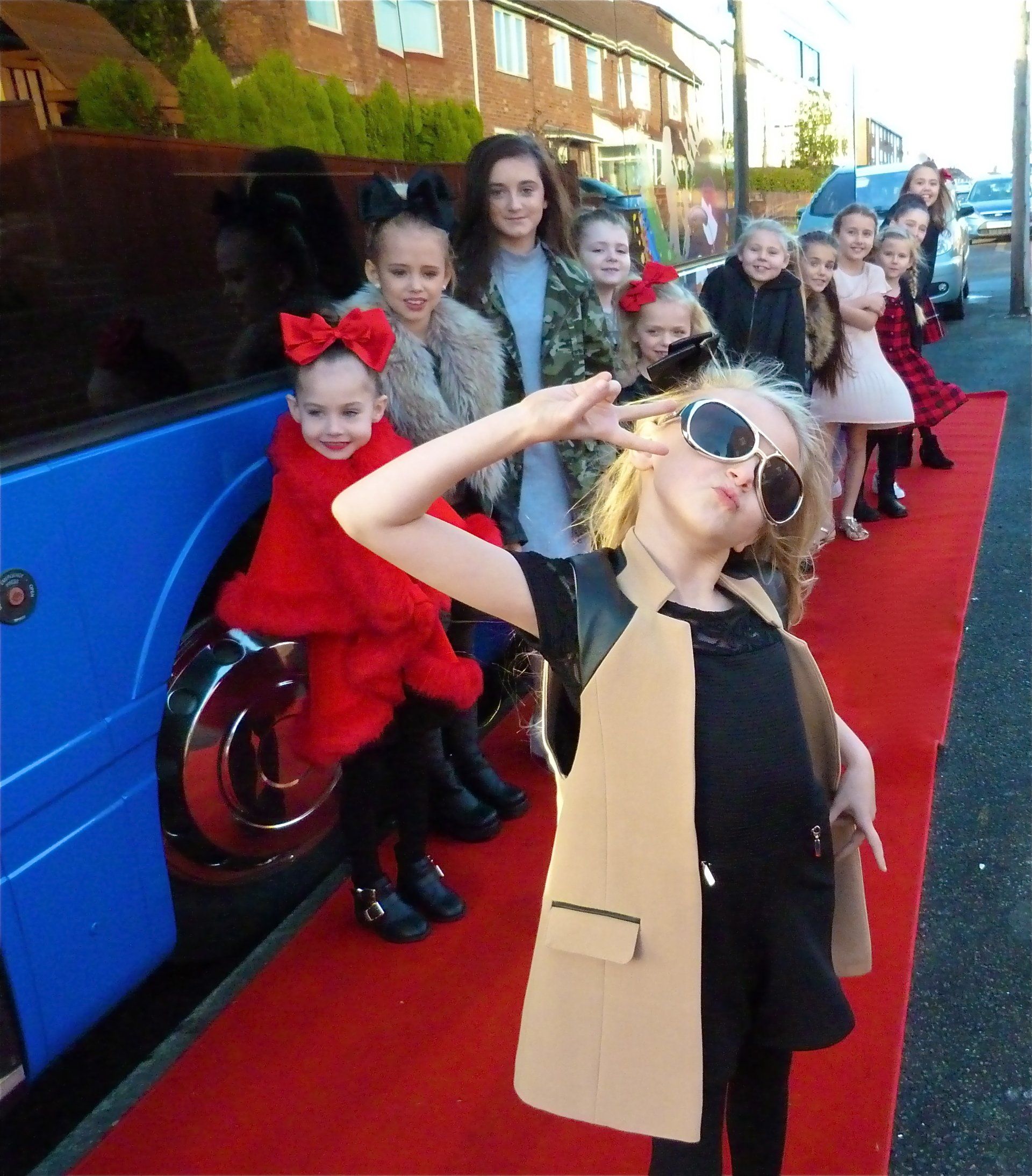 A group of young girls are standing on a red carpet in front of a blue bus