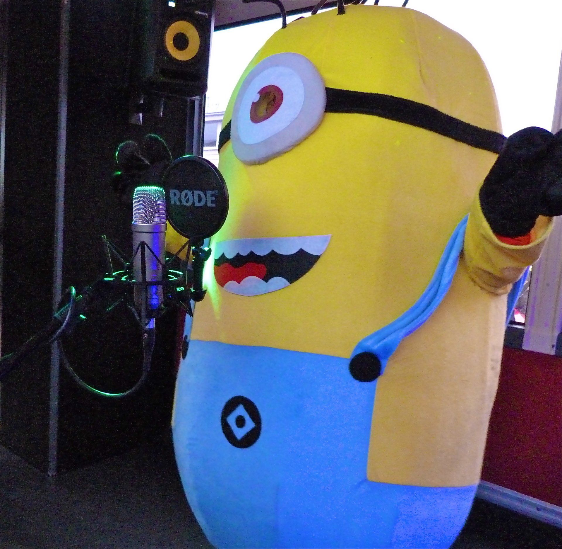 A stuffed minion is standing in front of a rode microphone