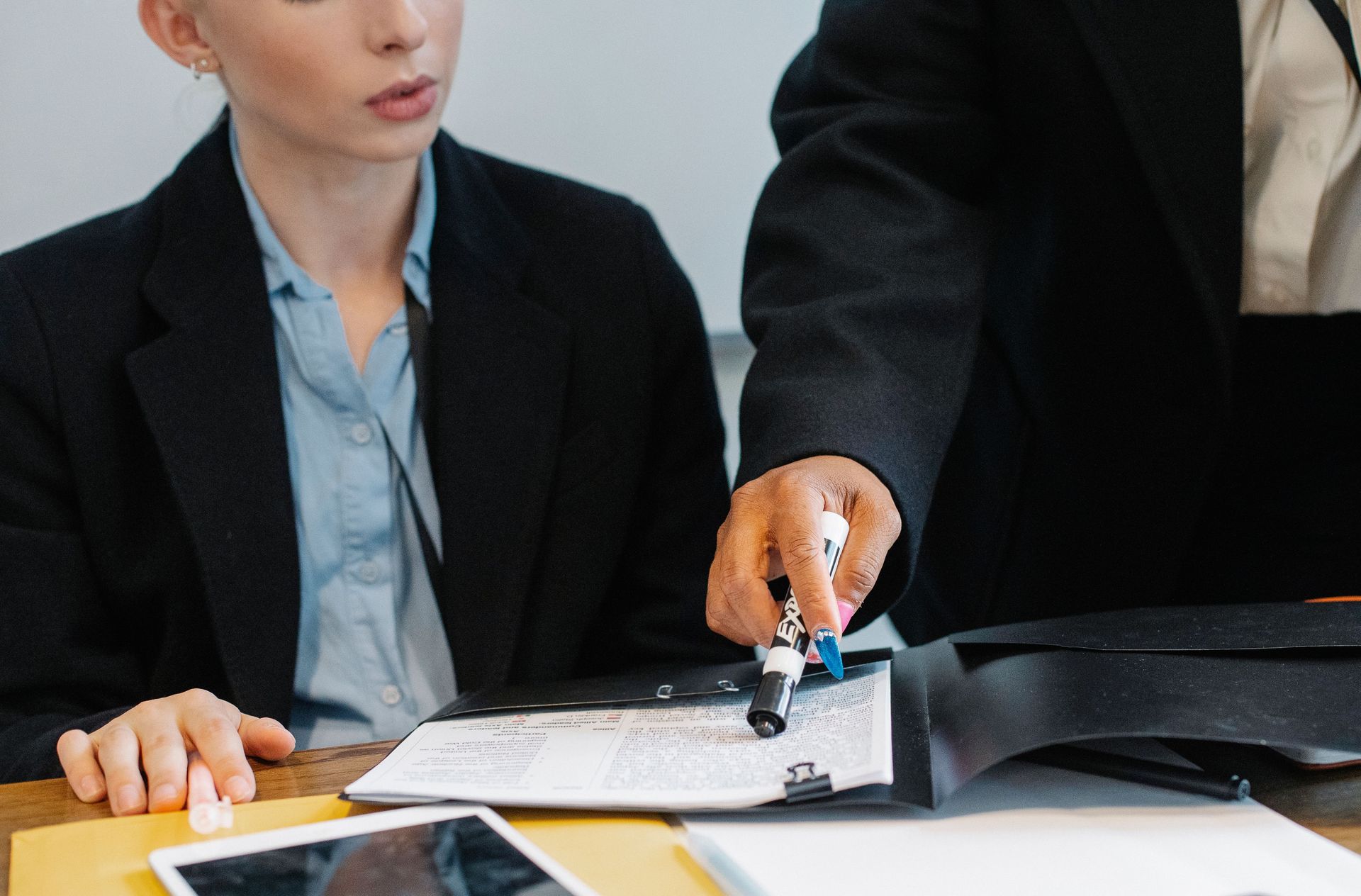 Two businesspeople reviewing documents at a desk, one pointing at a clipboard.