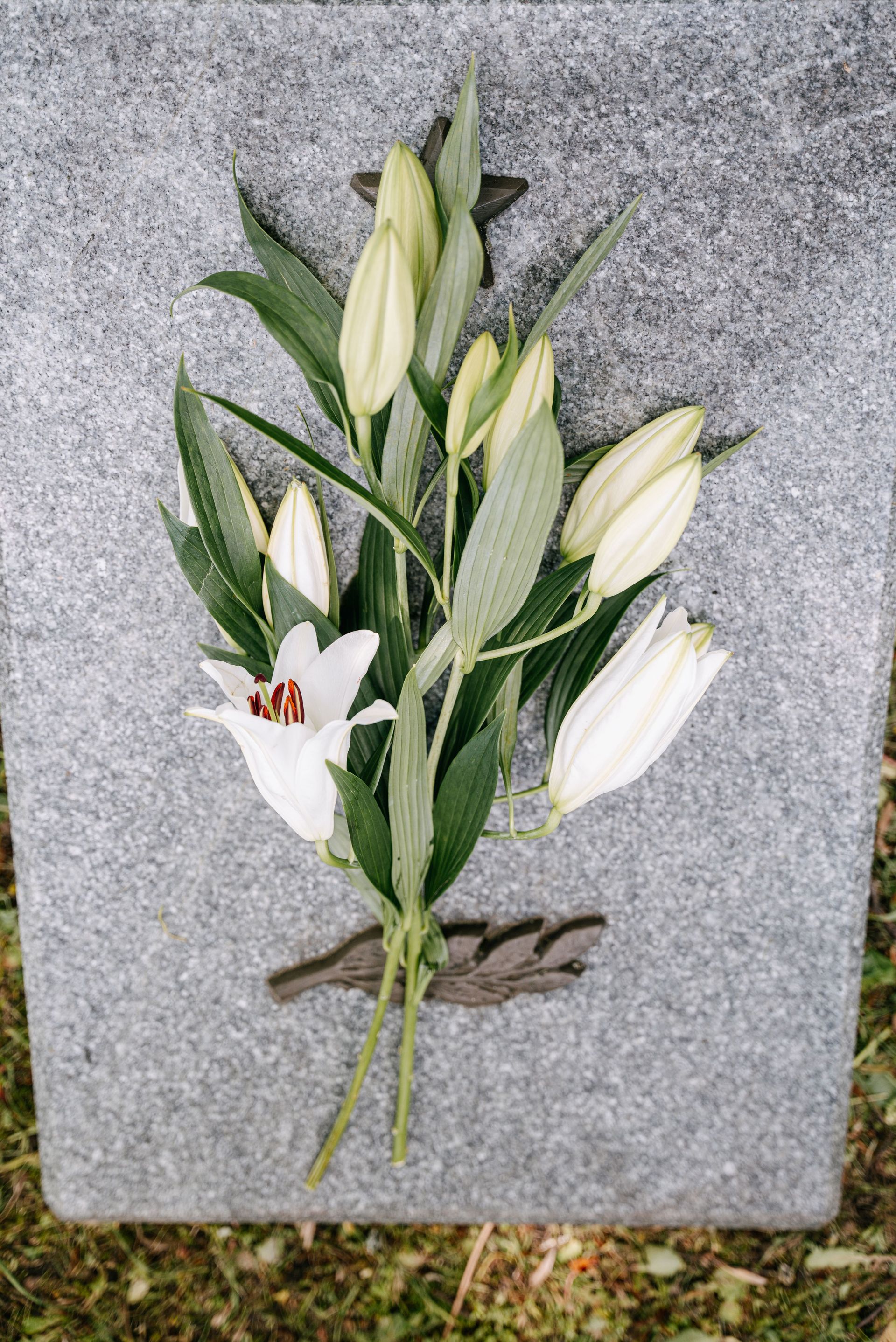 White lily bouquet with green leaves laid on a gray stone surface