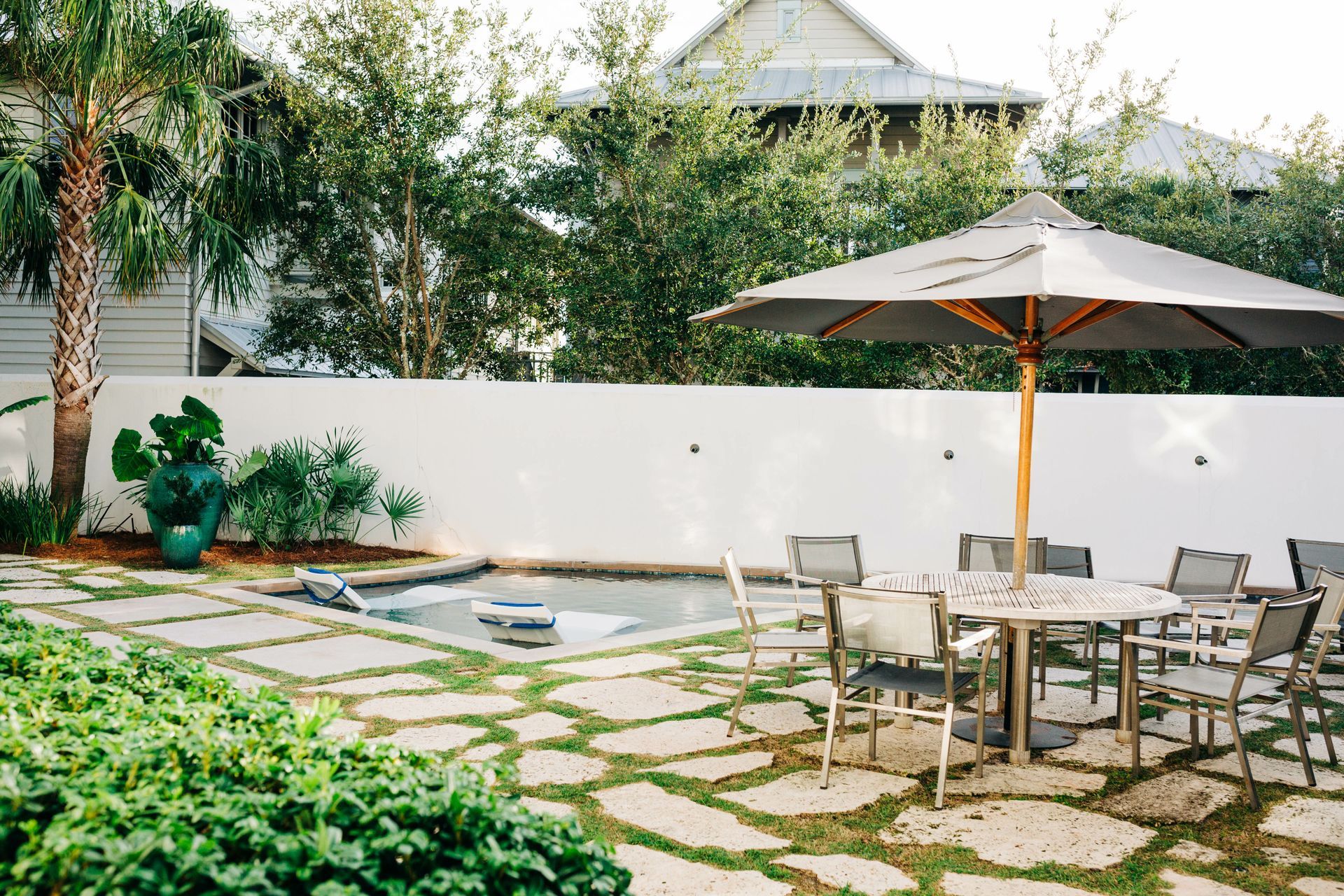 A patio with a table and chairs and an umbrella in front of a pool.