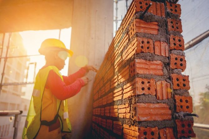 Construction worker laying bricks on a sunlit wall at a building site