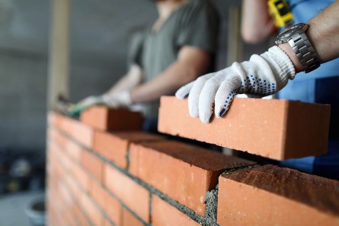 Gloved hands laying red bricks in a mortar wall on a construction site