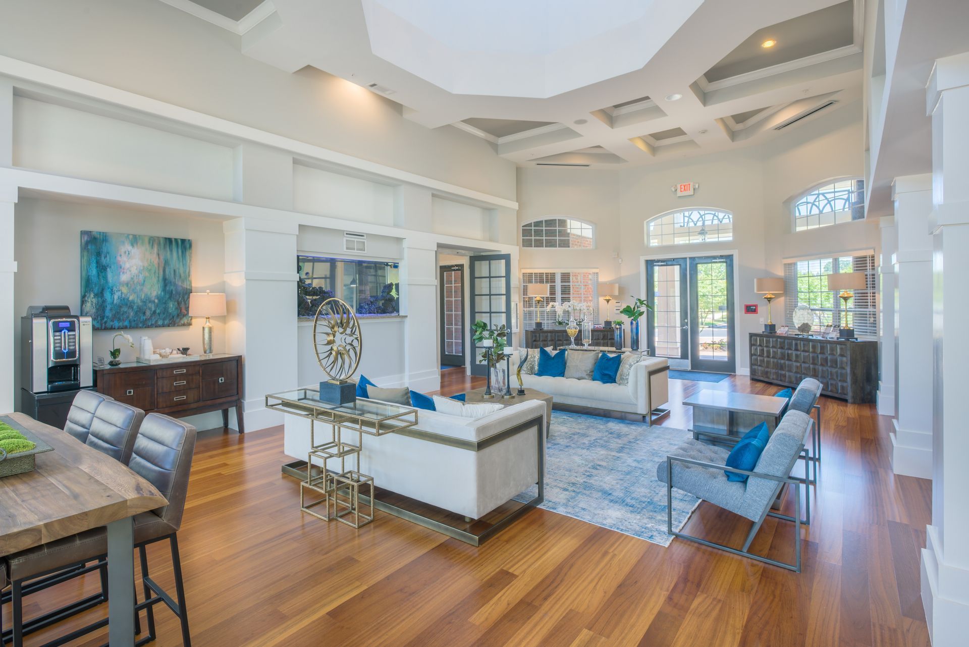 A bright, spacious apartment complex lobby with wood floors, modern white furniture, blue accents, and vaulted ceilings at The Vive at Kellswater.