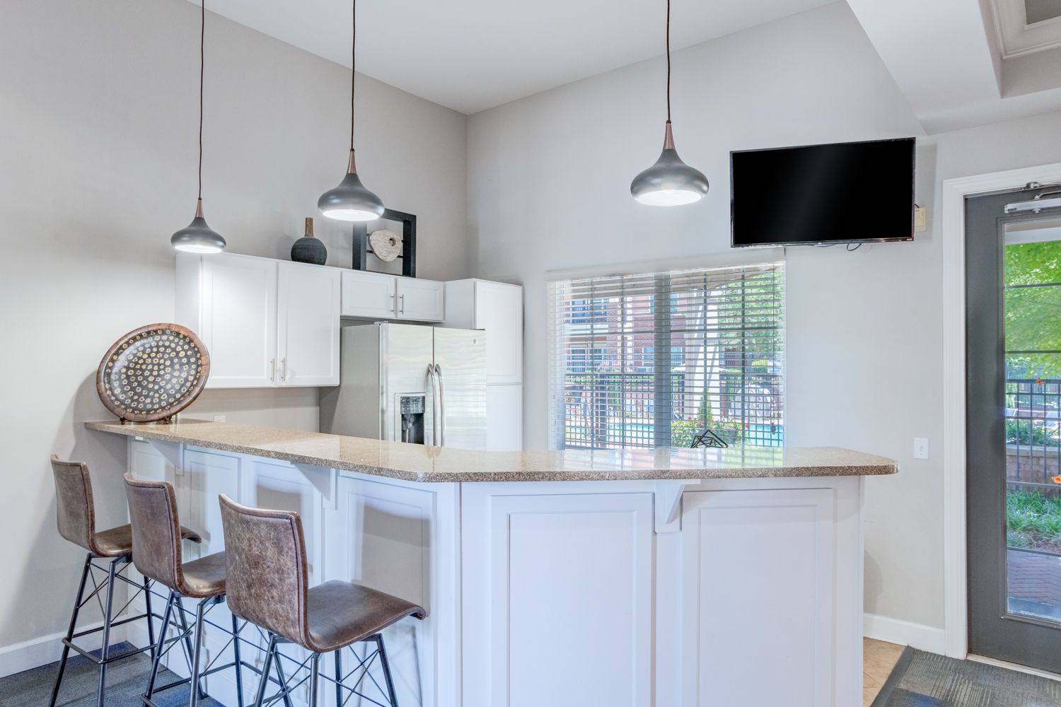 Kitchen bar with stools, granite counter, white cabinets, and TV at The Vive at Kellswater.