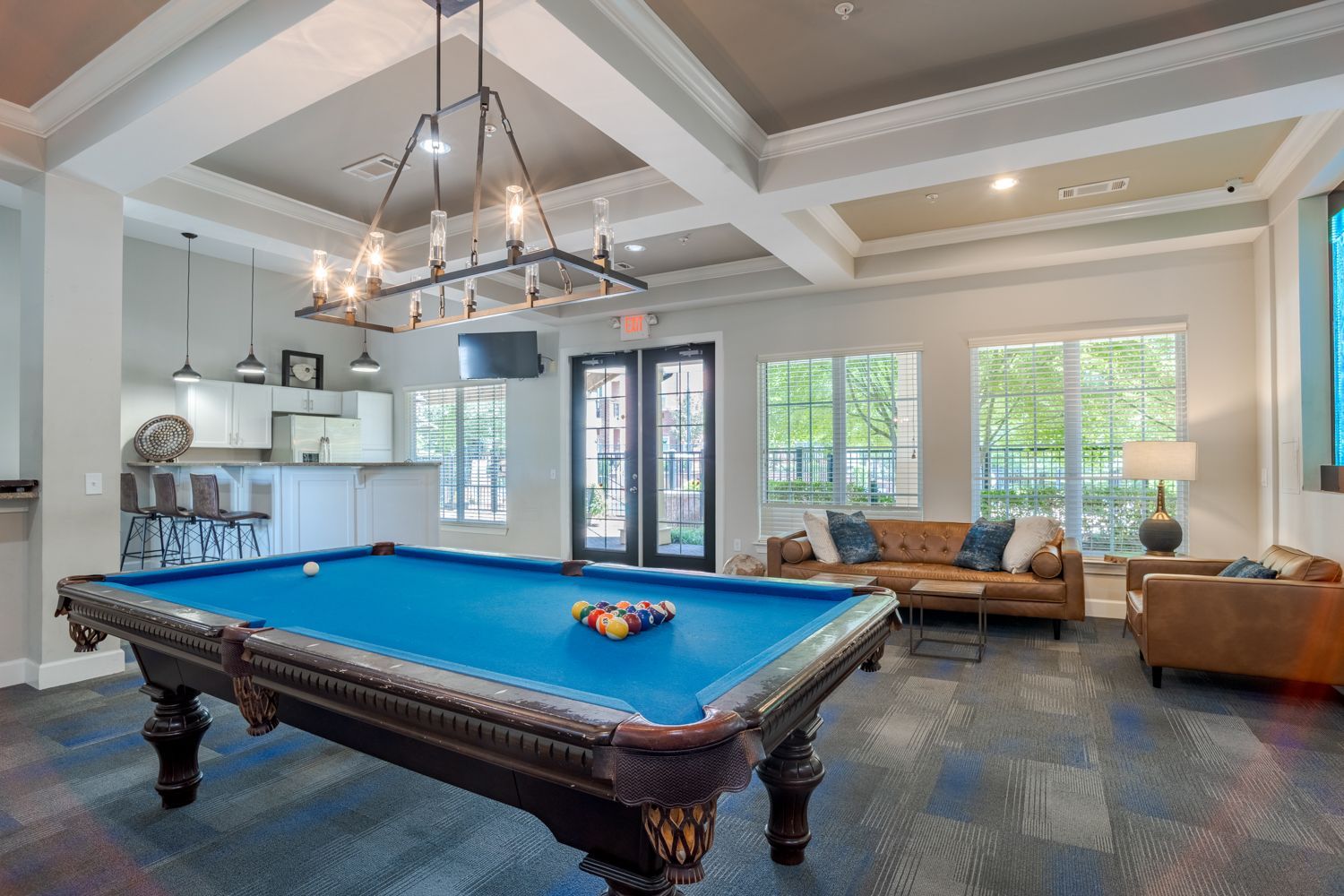 Pool table in a common area with seating, doors, windows, and a kitchen visible at The Vive at Kellswater.