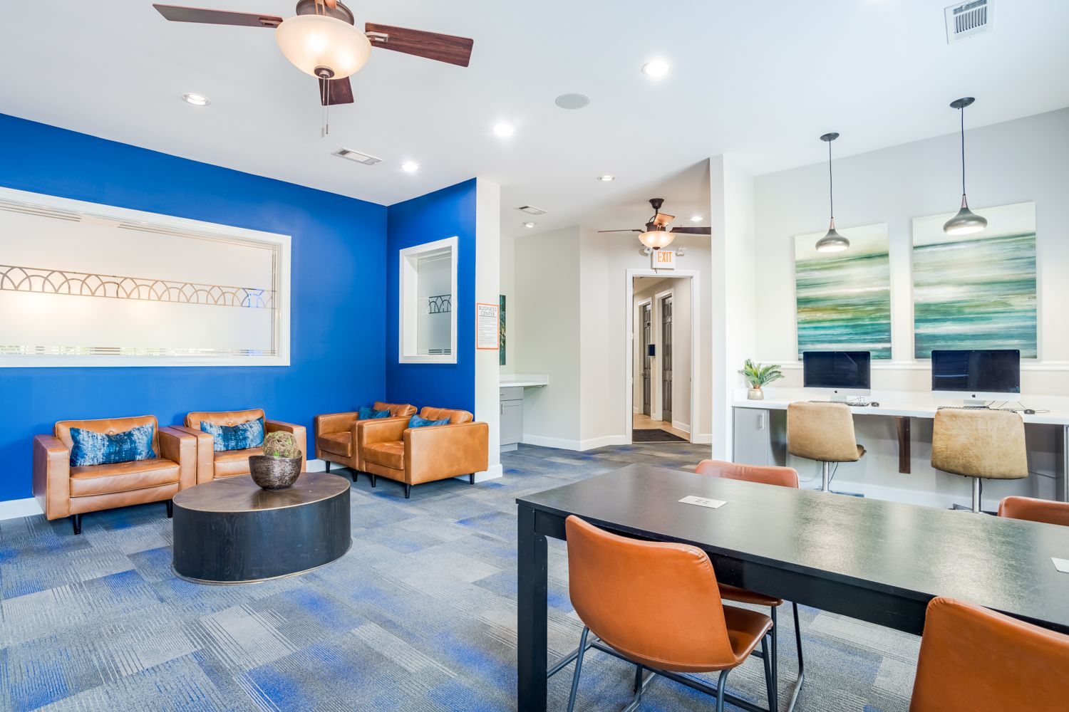 Lounge area with blue walls, brown leather chairs, a round coffee table, and a black table with orange chairs at The Vive at Kellswater.