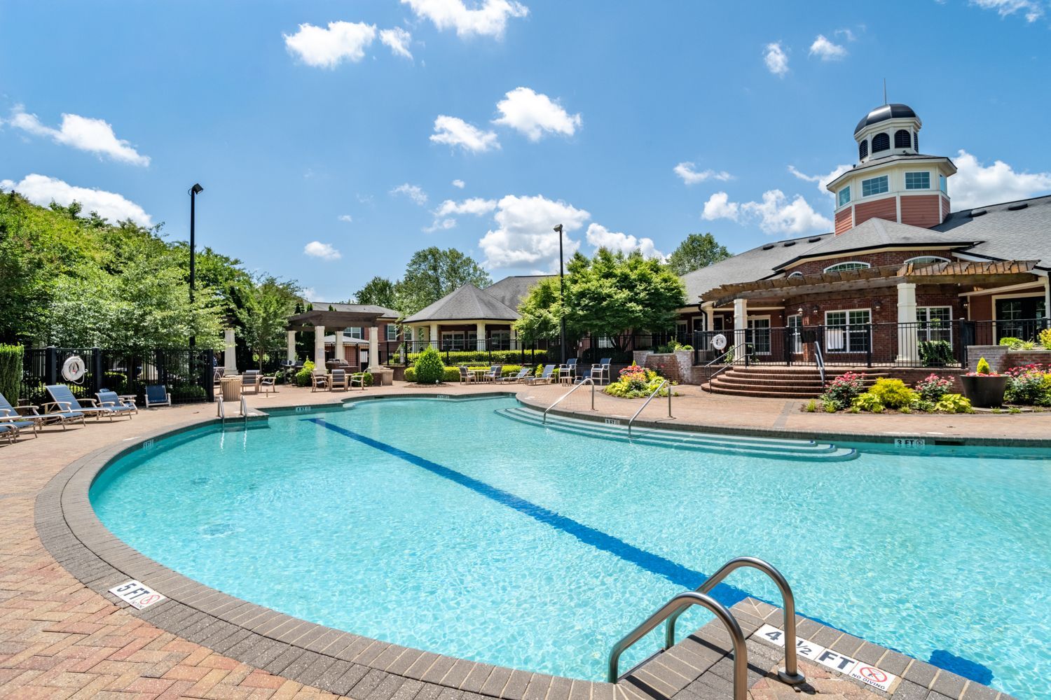 Swimming pool with brick edging, lounge chairs, and a clubhouse under a blue sky at The Vive at Kellswater.