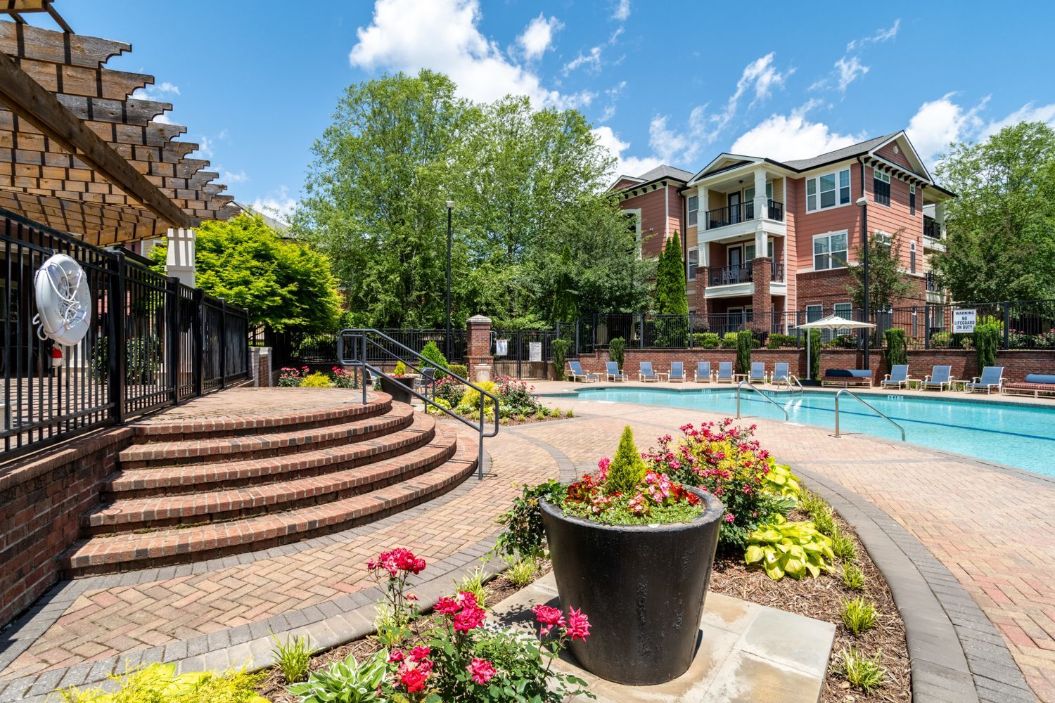 A brick patio leads to a swimming pool at an apartment complex under a sunny sky at The Vive at Kellswater.
