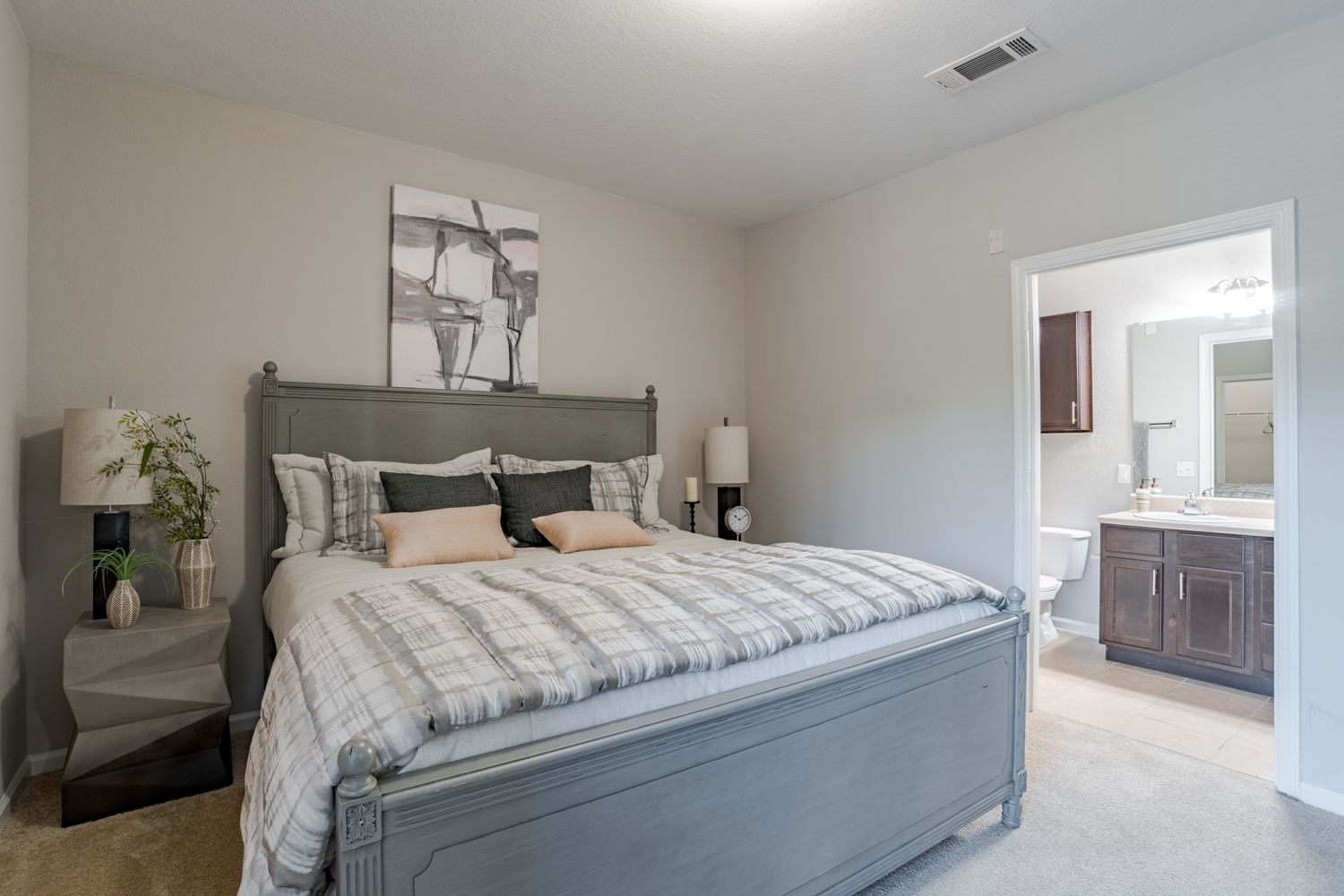 Bedroom with gray bed, nightstands, and artwork; bathroom visible through doorway at The Vive at Kellswater.