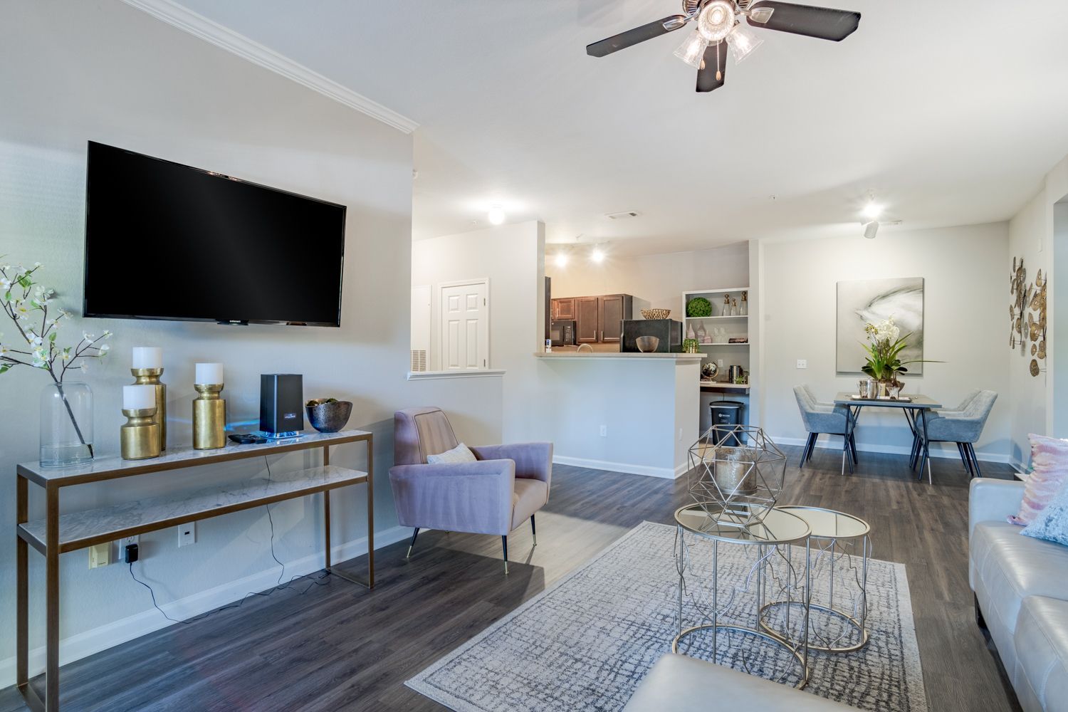 Living room with mounted TV, purple chair, kitchen view, dining area, gray walls, dark wood floors at The Vive at Kellswater.