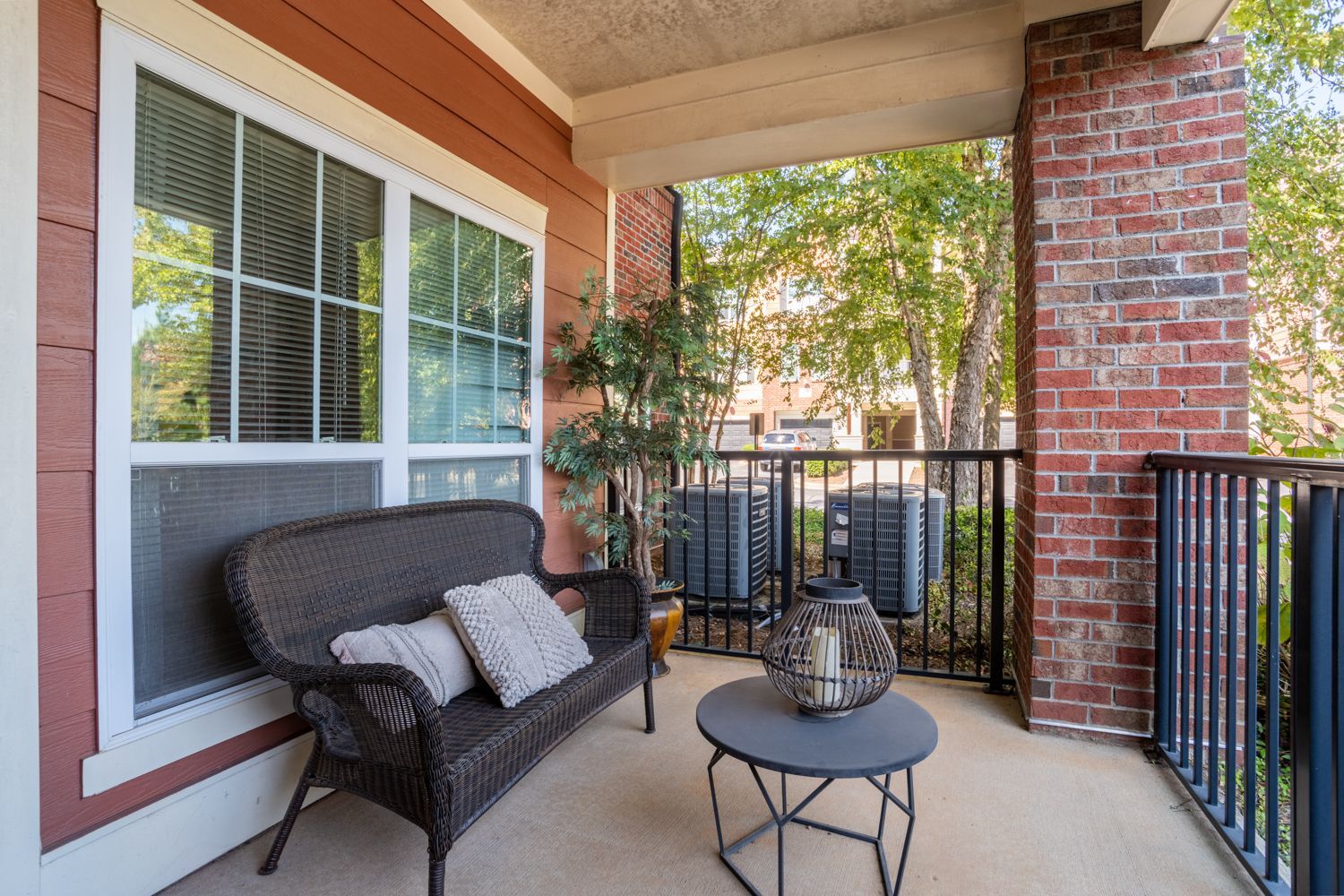 Balcony with wicker furniture, brick pillar, and view of trees at The Vive at Kellswater.