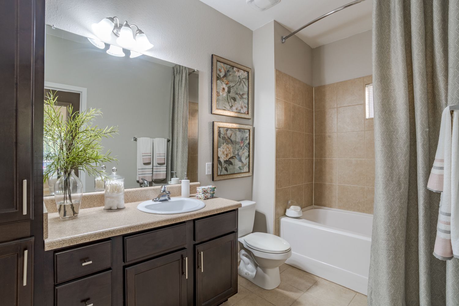 Bathroom with dark brown vanity, white sink, beige tile, and shower curtain at The Vive at Kellswater.