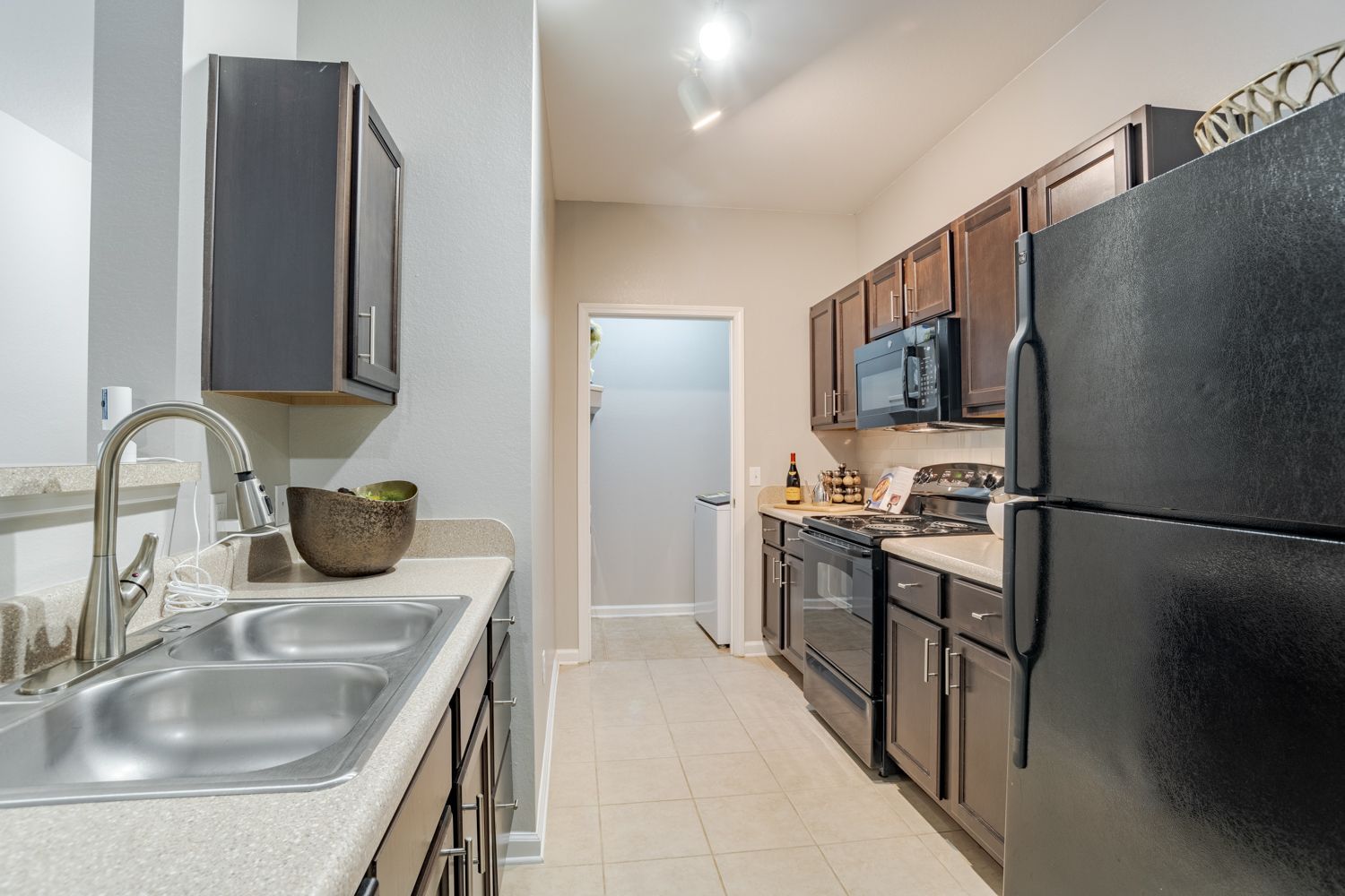Kitchen with gray cabinets, black appliances, stainless steel sink, and light-colored tile at The Vive at Kellswater.