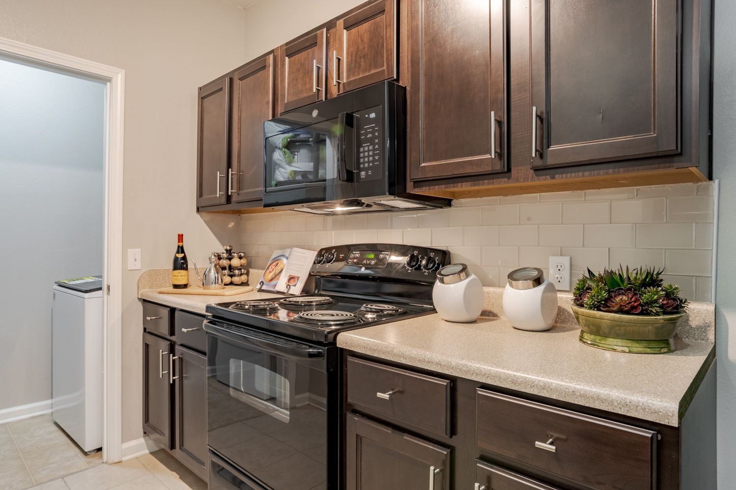Kitchen with dark brown cabinets, black appliances, and off-white countertops at The Vive at Kellswater.