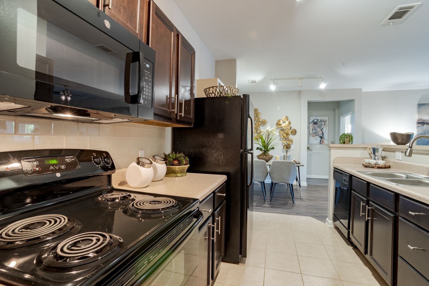 Kitchen with black appliances and dark cabinets, leading to a dining area at The Vive at Kellswater.