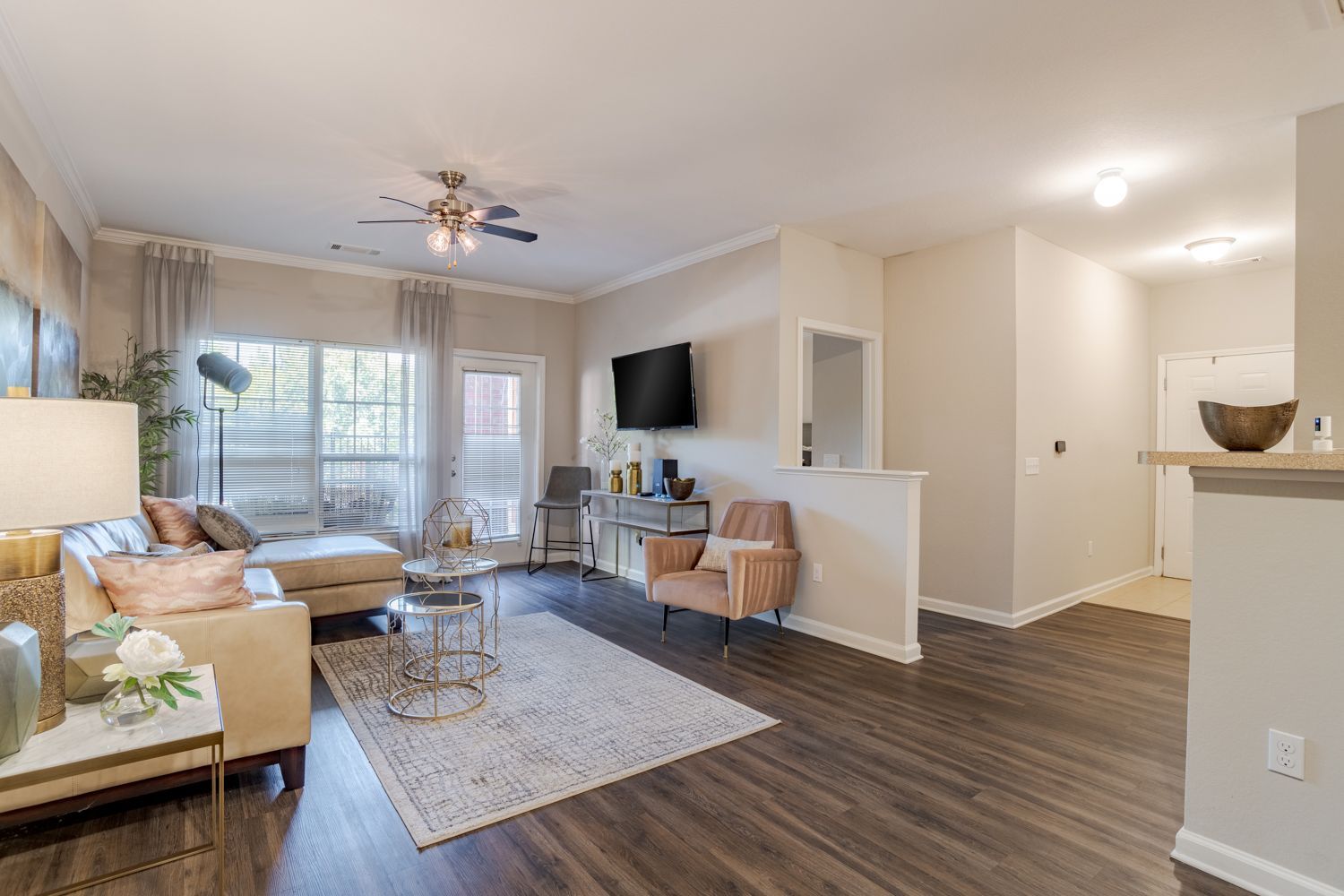 Cozy living room with tan sectional, rug, TV, and pink armchair, and dark wood floors at The Vive at Kellswater.