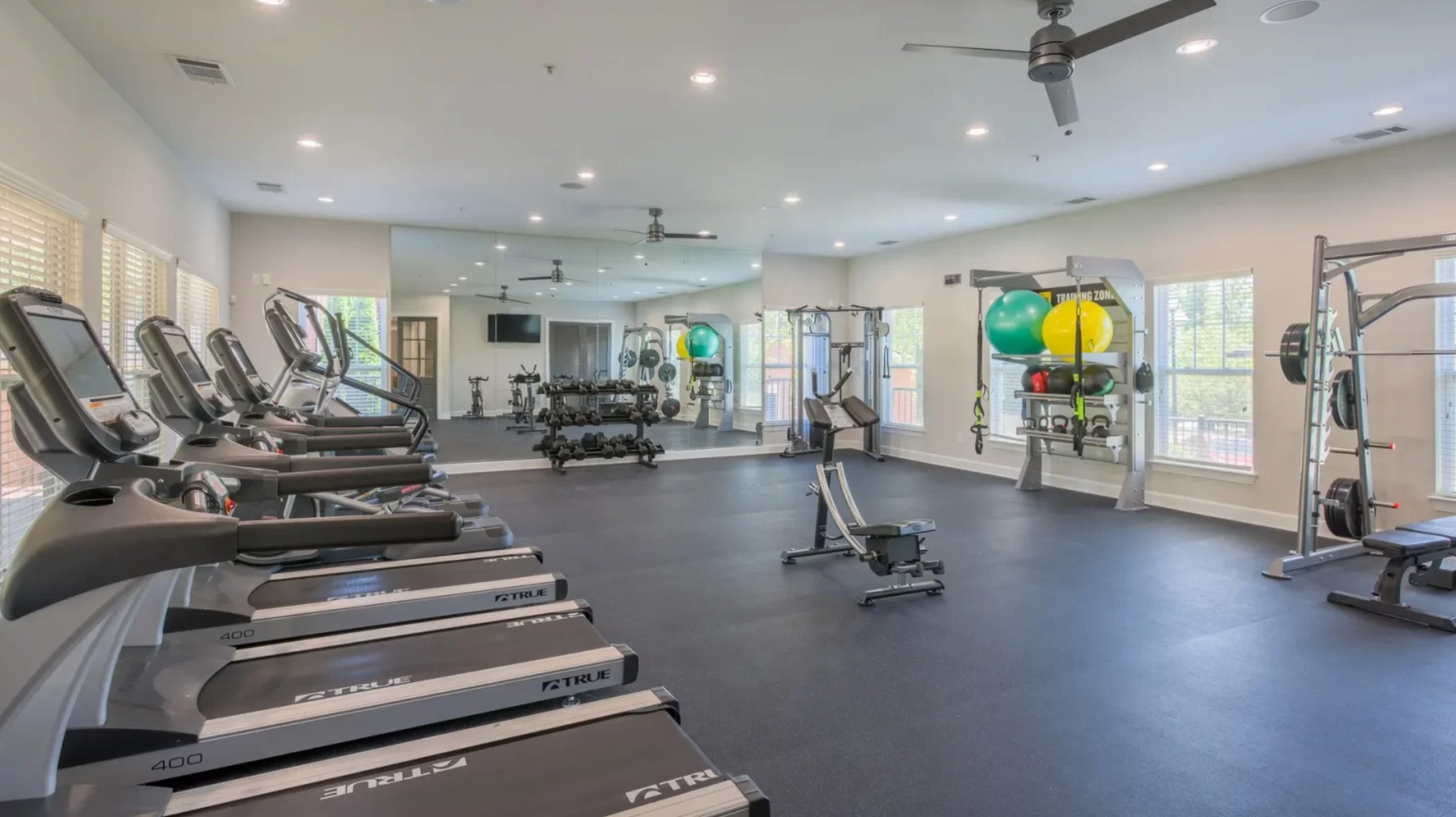 A bright, spacious indoor fitness center with rows of treadmills, exercise balls, and weight equipment at The Vive at Kellswater.
