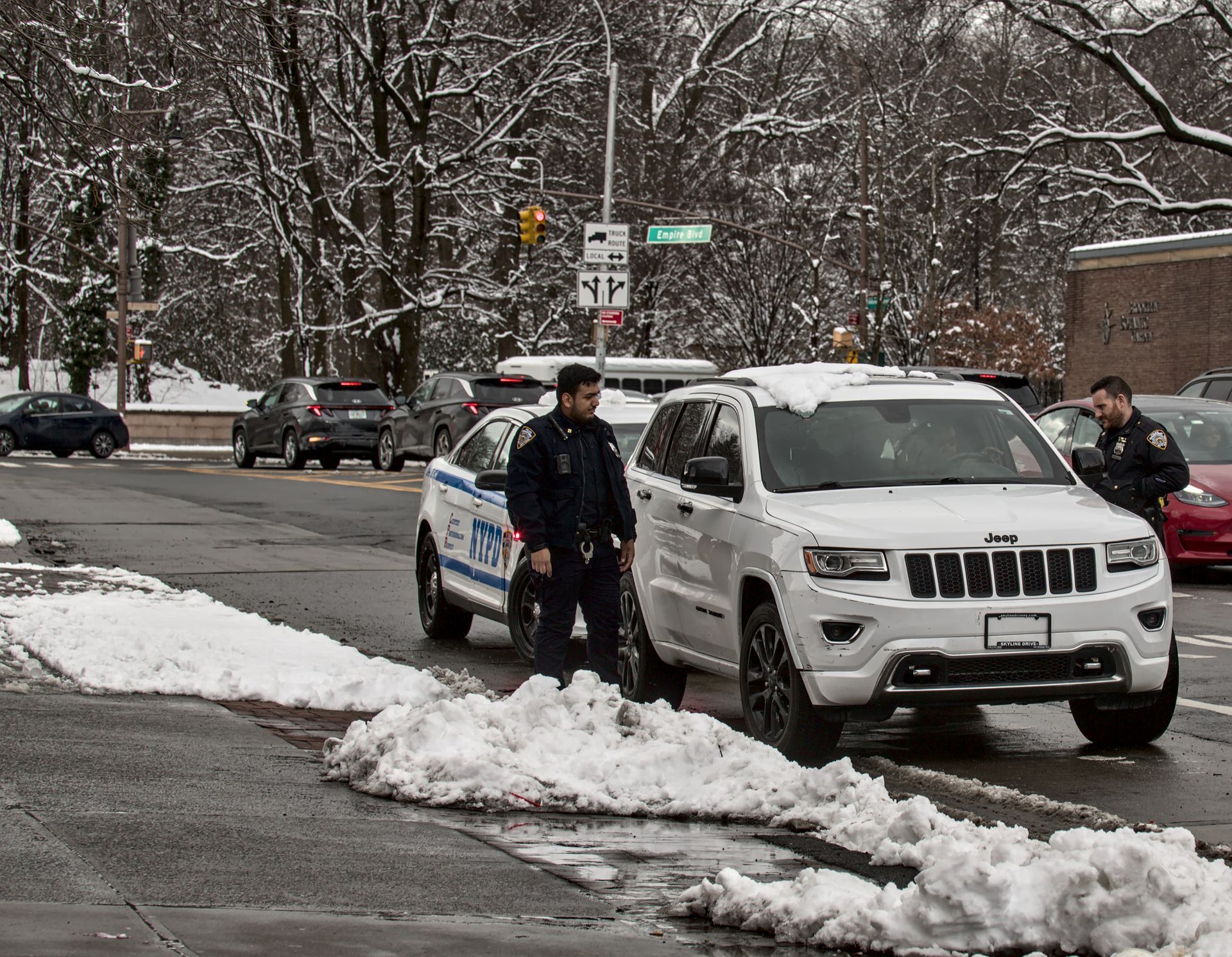 A police officer is standing next to a white jeep parked in the snow.