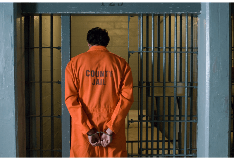 Man in orange jumpsuit with hands behind his back.