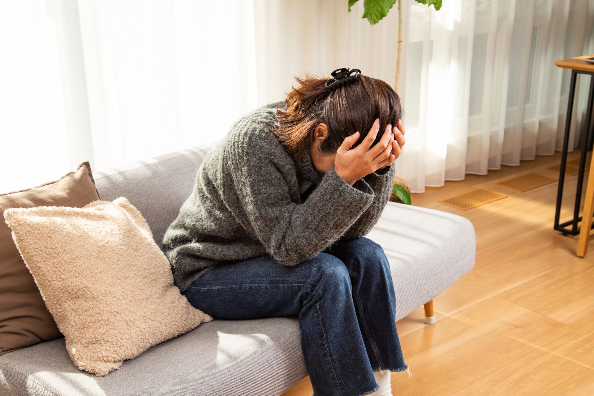 Person sitting on a couch with head in hands in a bright living room