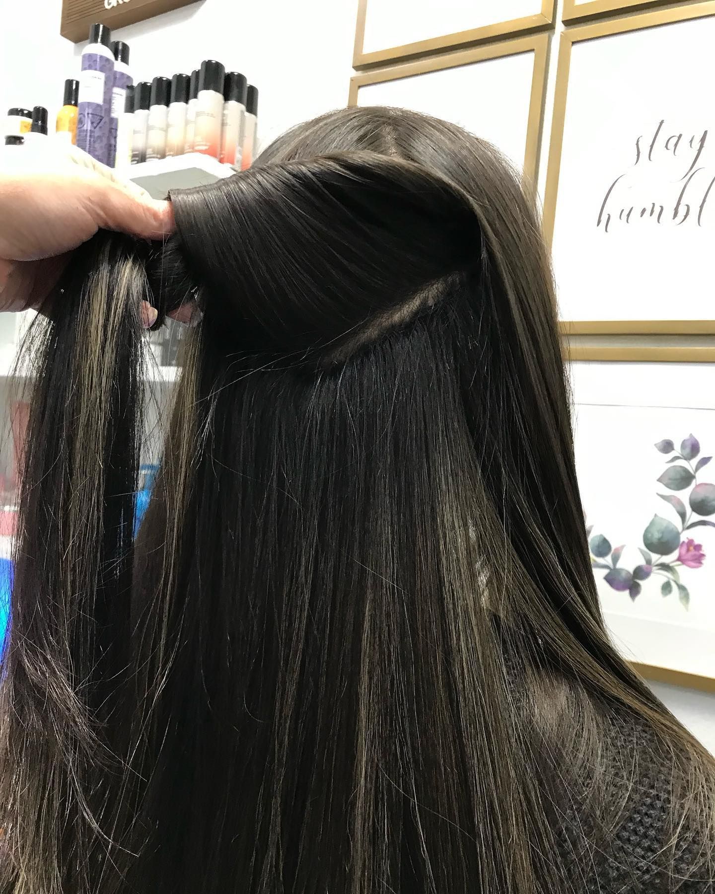 Close-up of hair being styled. A hand holds the hair up, revealing a sectioned area, likely for a braid.