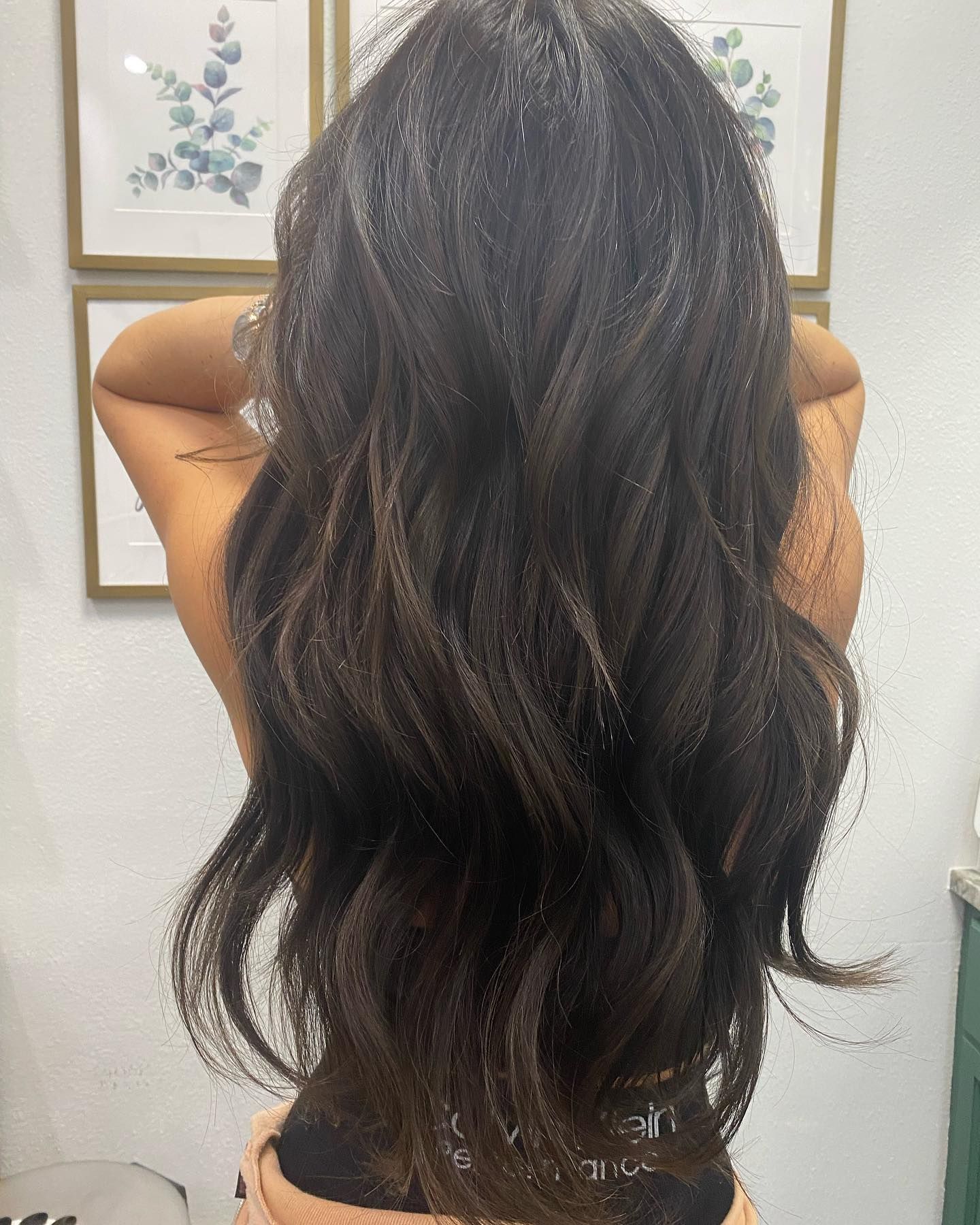 Woman with long wavy dark hair, back to the camera, arms up.