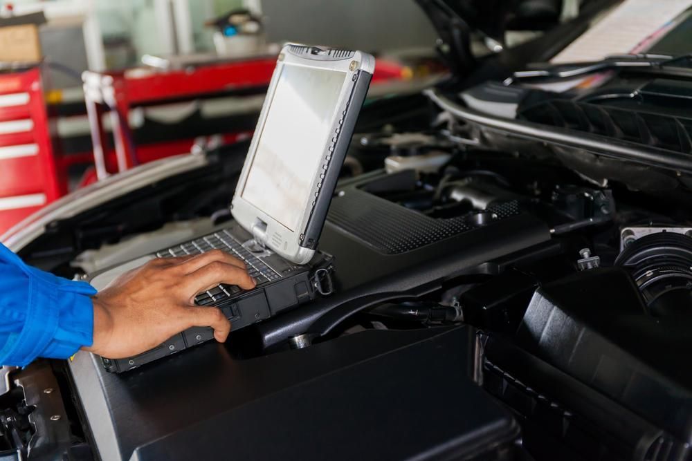 A Mechanic Is Using a Laptop Computer Under the Hood of A Car — Lismore Car Repairs in Lismore, NSW