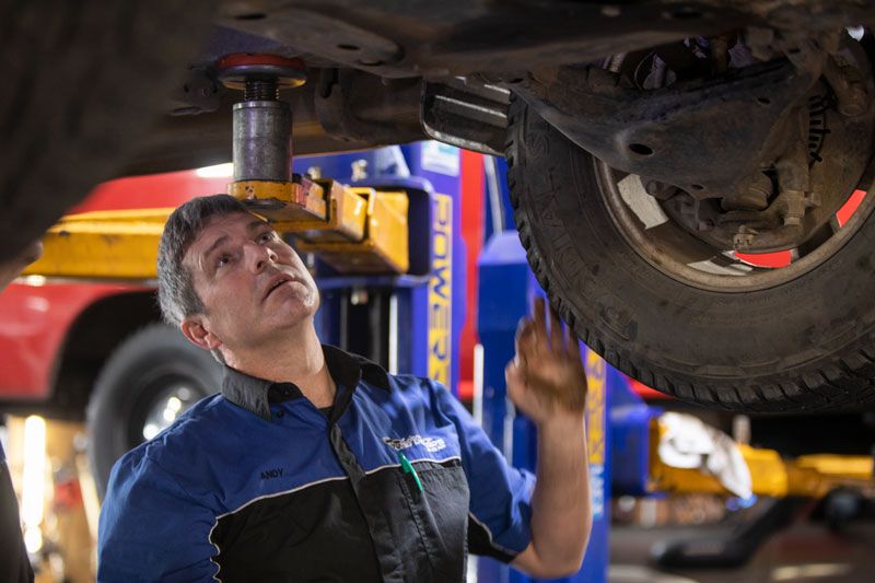 A Man Is Working Under a Car on A Lift in A Garage — Lismore Car Repairs in Lismore, NSW