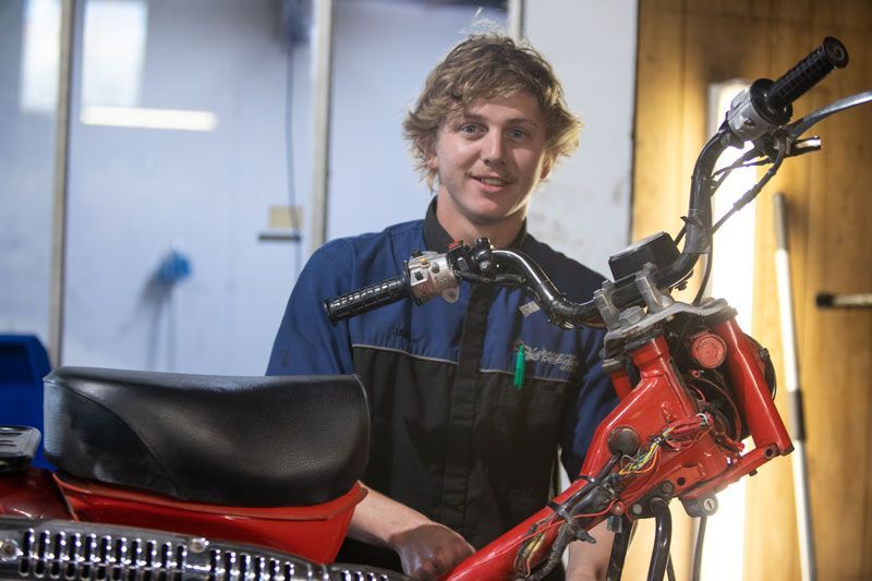 A Man Is Standing Next to A Red Motorcycle in A Garage — Lismore Car Repairs in Lismore, NSW