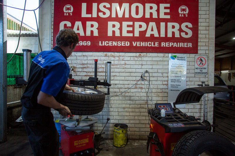 A Man Is Changing a Tire in Front of A Sign that Says Lismore Car Repairs — Lismore Car Repairs in Lismore, NSW