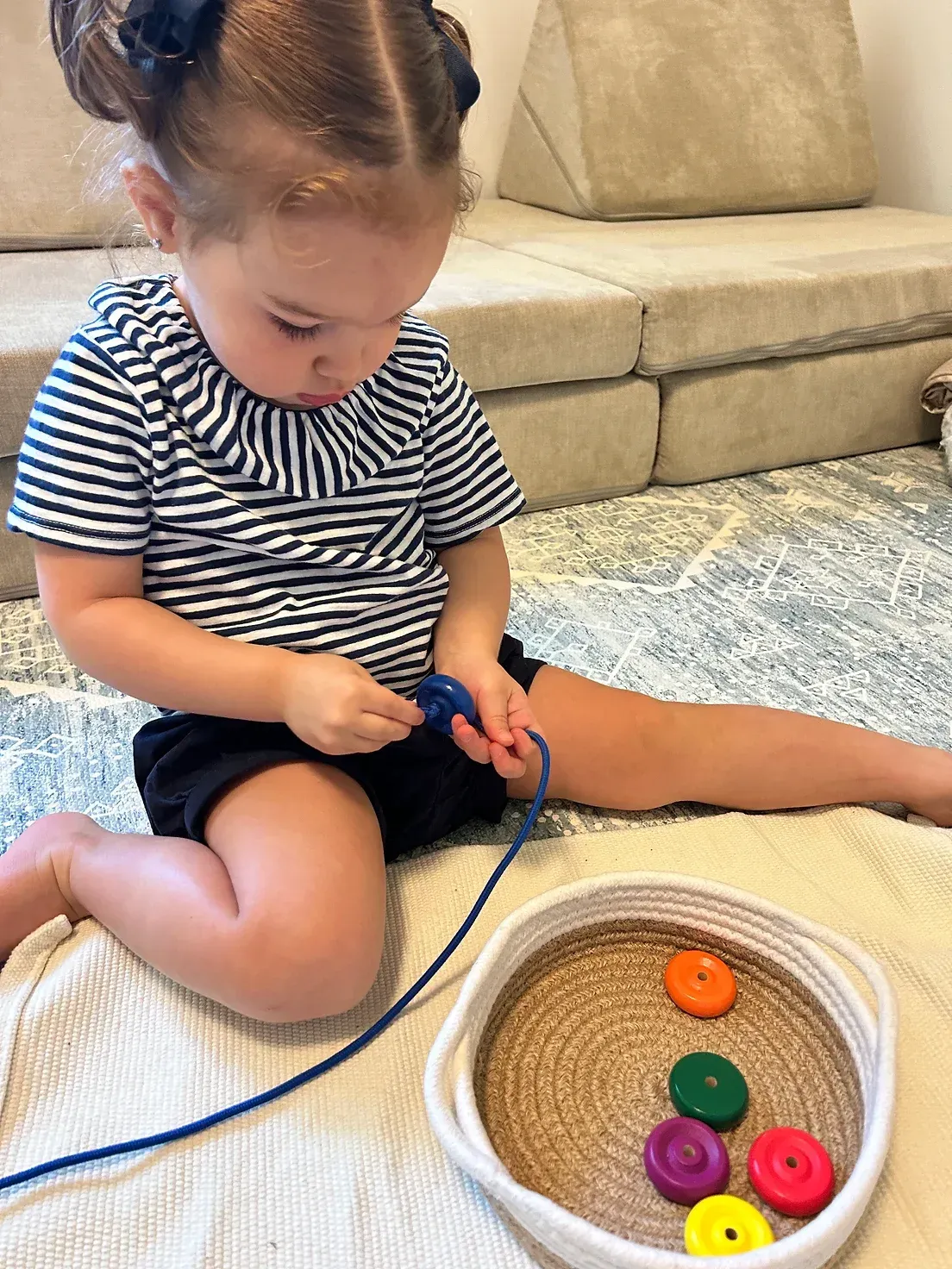 A little girl is sitting on the floor playing with a string and buttons.