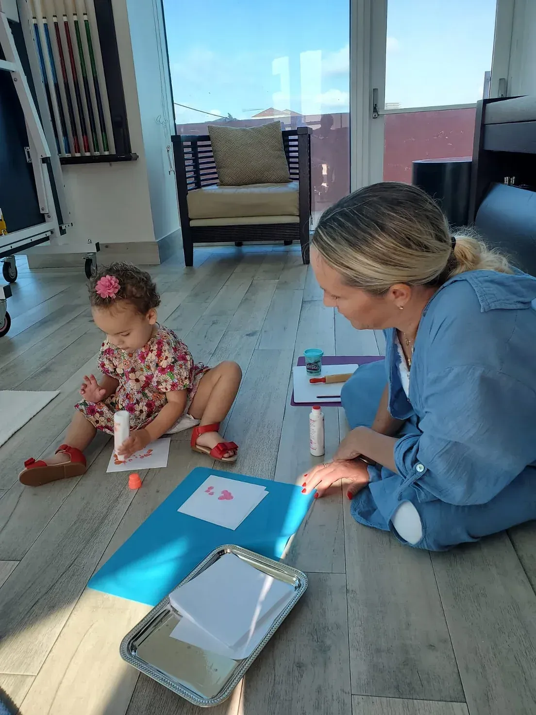 A woman and a little girl are sitting on the floor playing with glue.
