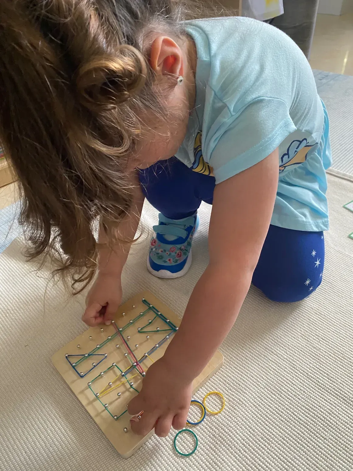 A little girl is kneeling on the floor playing with a wooden board.