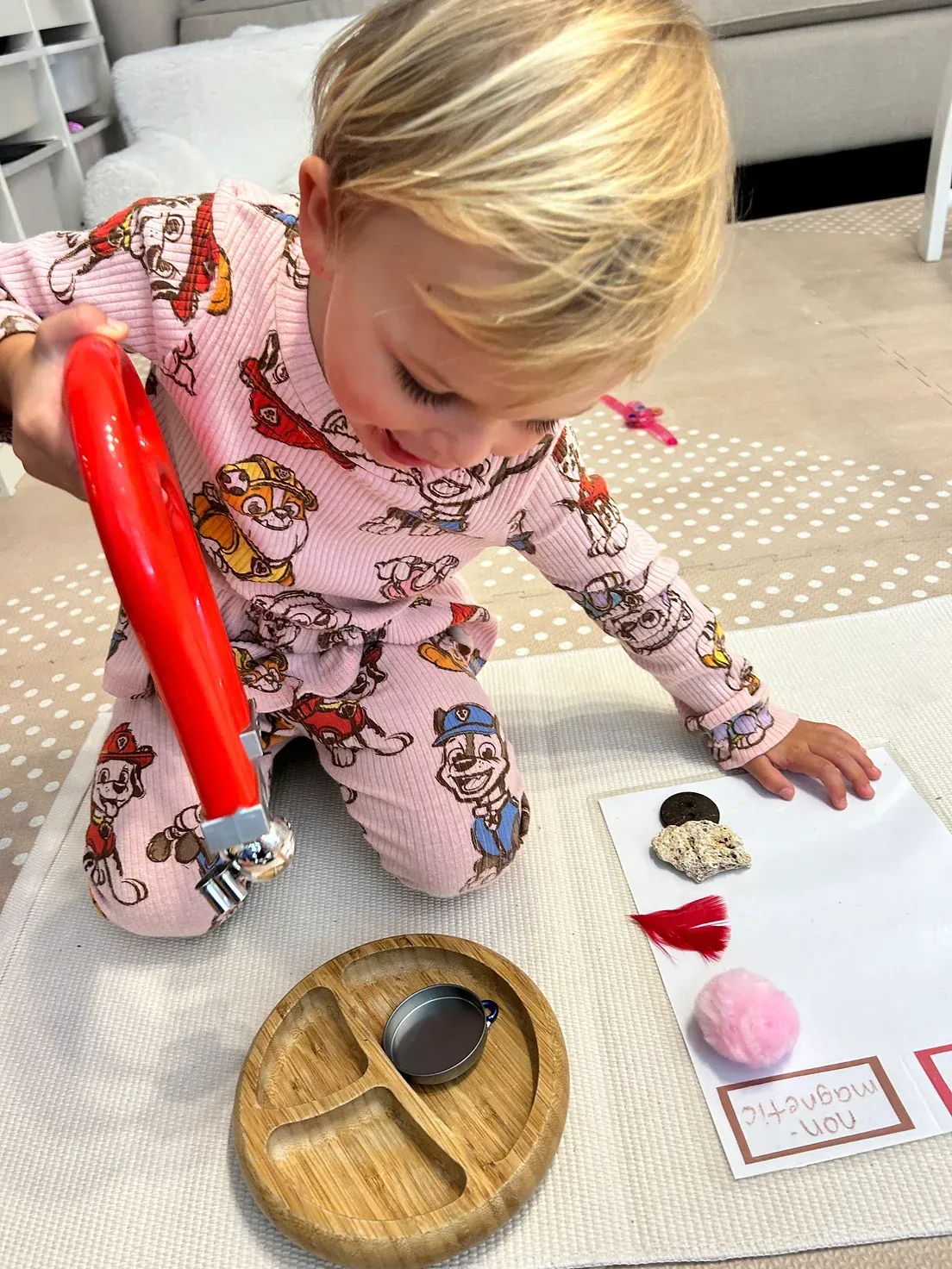 A little girl is kneeling on the floor playing with a spoon and a plate.