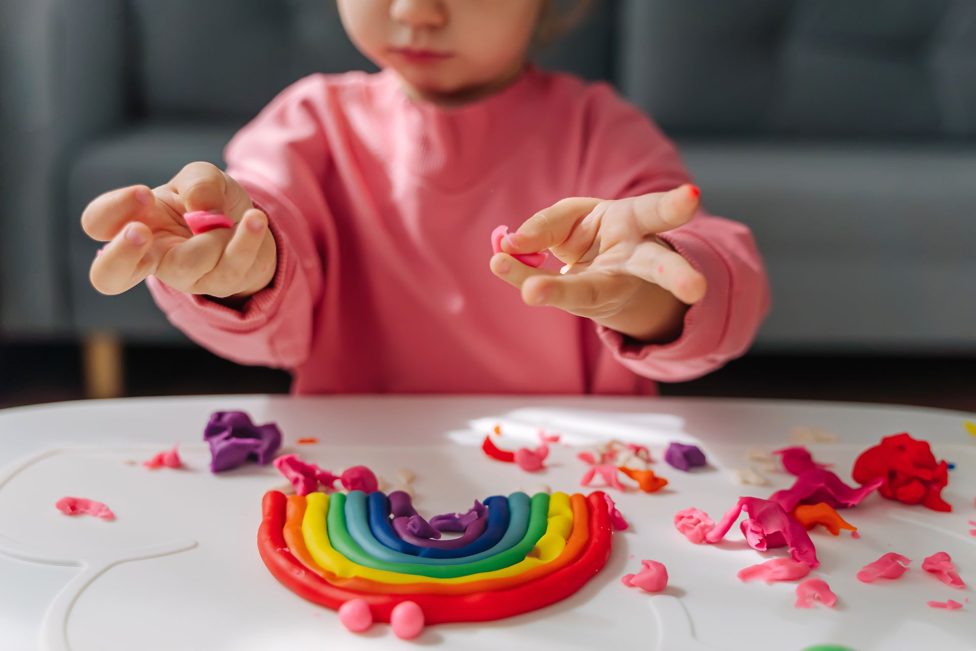 A little girl is playing with play dough at a table.