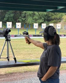 Person wearing ear protection aiming a handgun at a shooting range target line