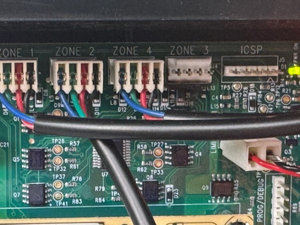 Close-up of a green circuit board with labeled zone connectors, wires, and electronic components.